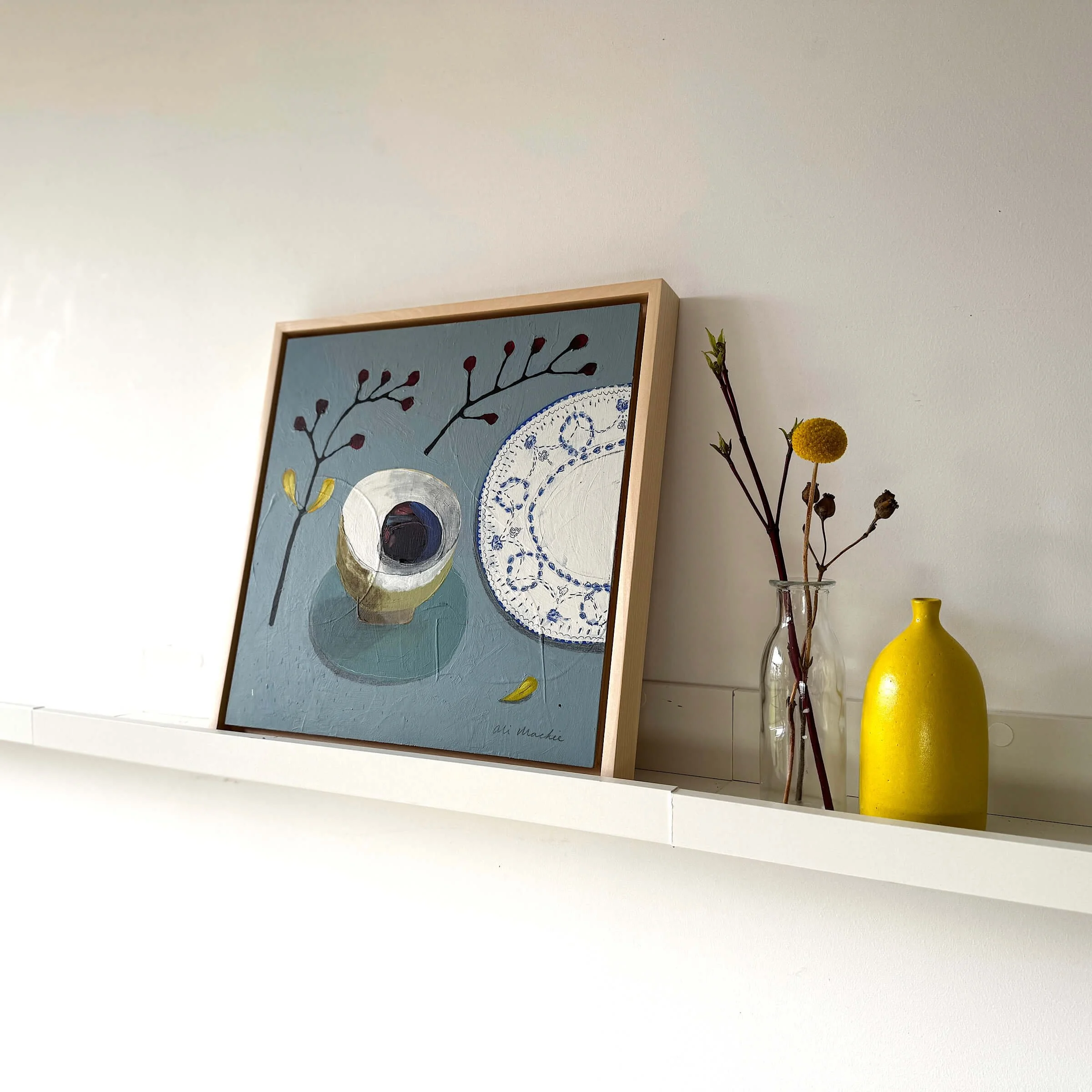 Original still life painting Join Me at the Table by Ali Mackie Art on a white shelf next to a yellow vase.