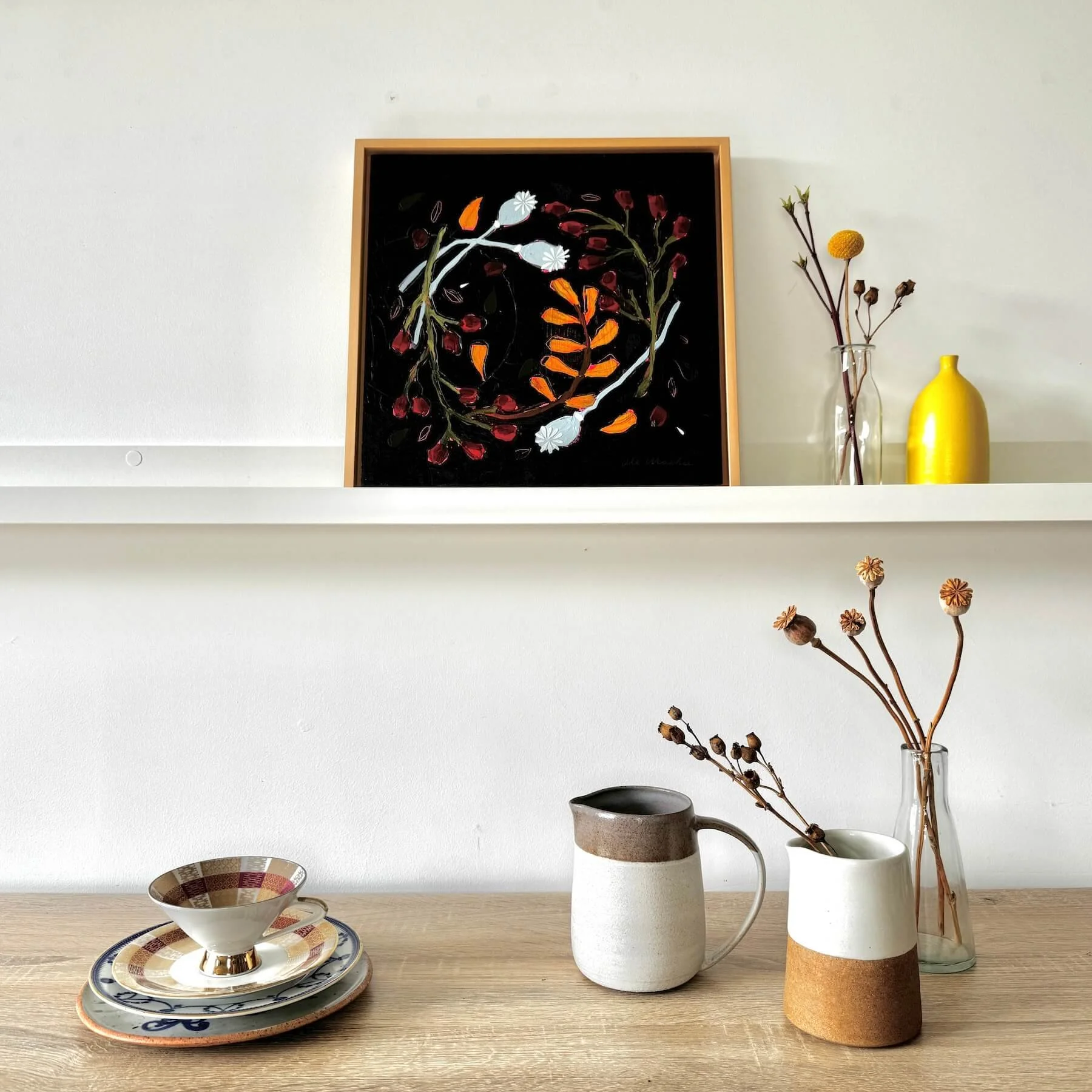 Styled interior view featuring the framed painting Wilda by Ali Mackie Art on a floating shelf above a table set with ceramic pitchers and a patterned teacup.