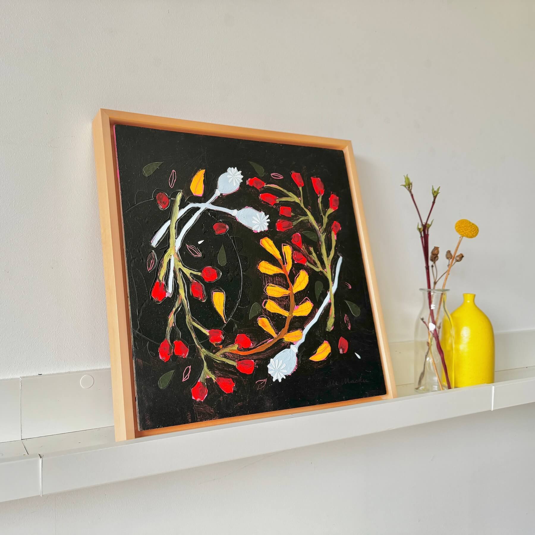 Angled view of the framed painting Wilda by Ali Mackie Art on a white ledge, showing white poppy seed pods and vibrant red berries on a black canvas background.