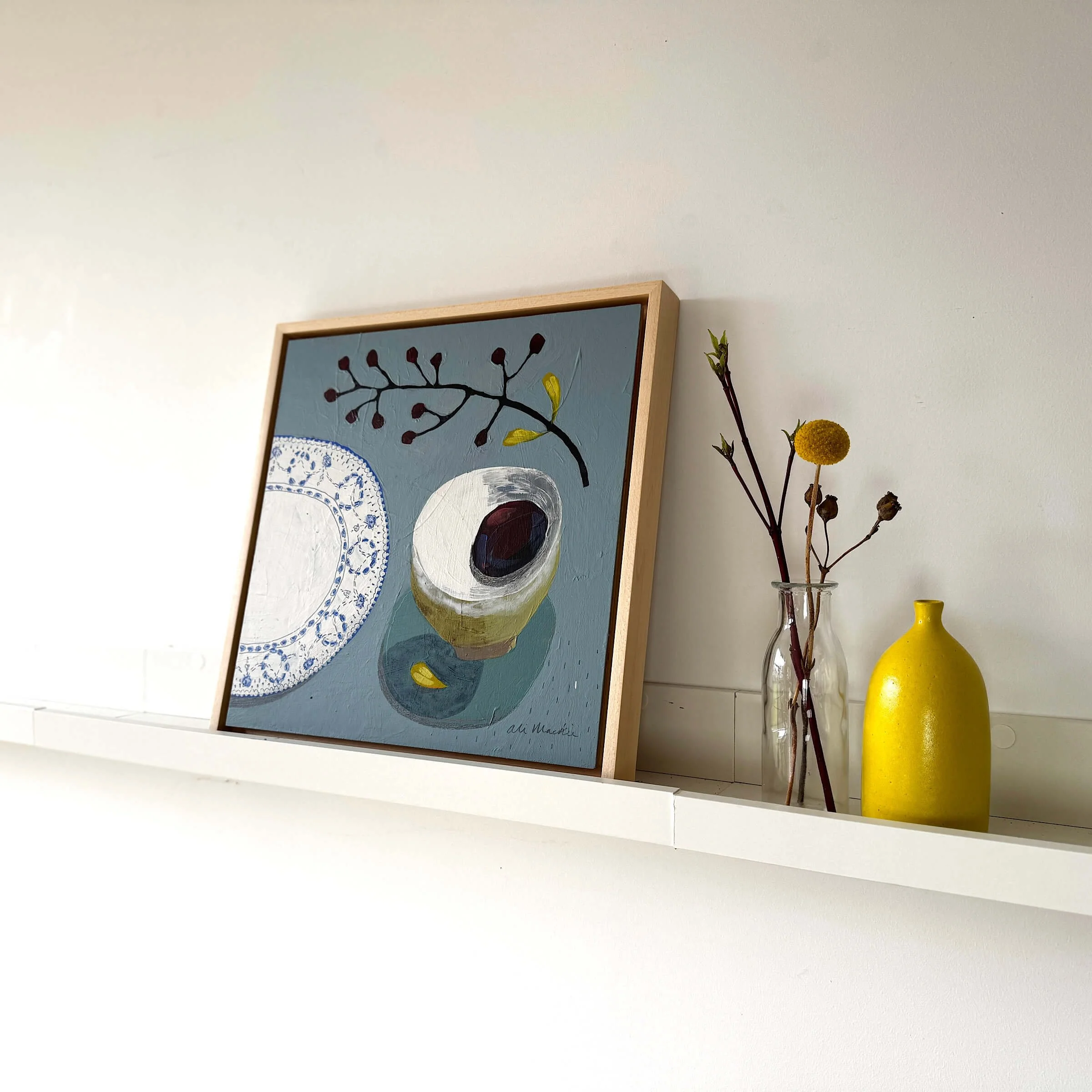 Original still life painting Lets Sit Together by Ali Mackie Art styled on a floating wall shelf next to a yellow vase.