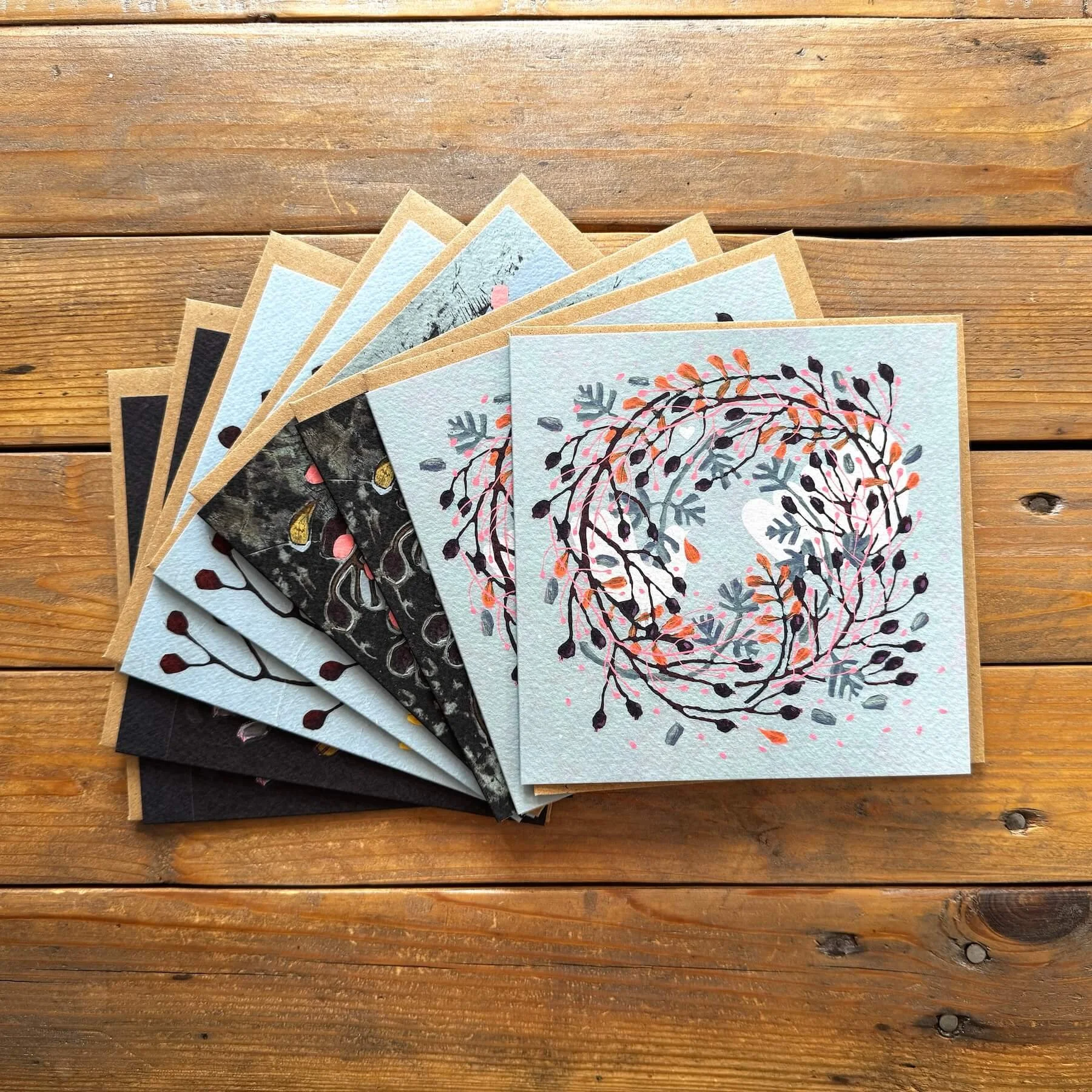 Fan display of 8 festive botanical wreath greeting cards showing four original hand-painted abstract designs.