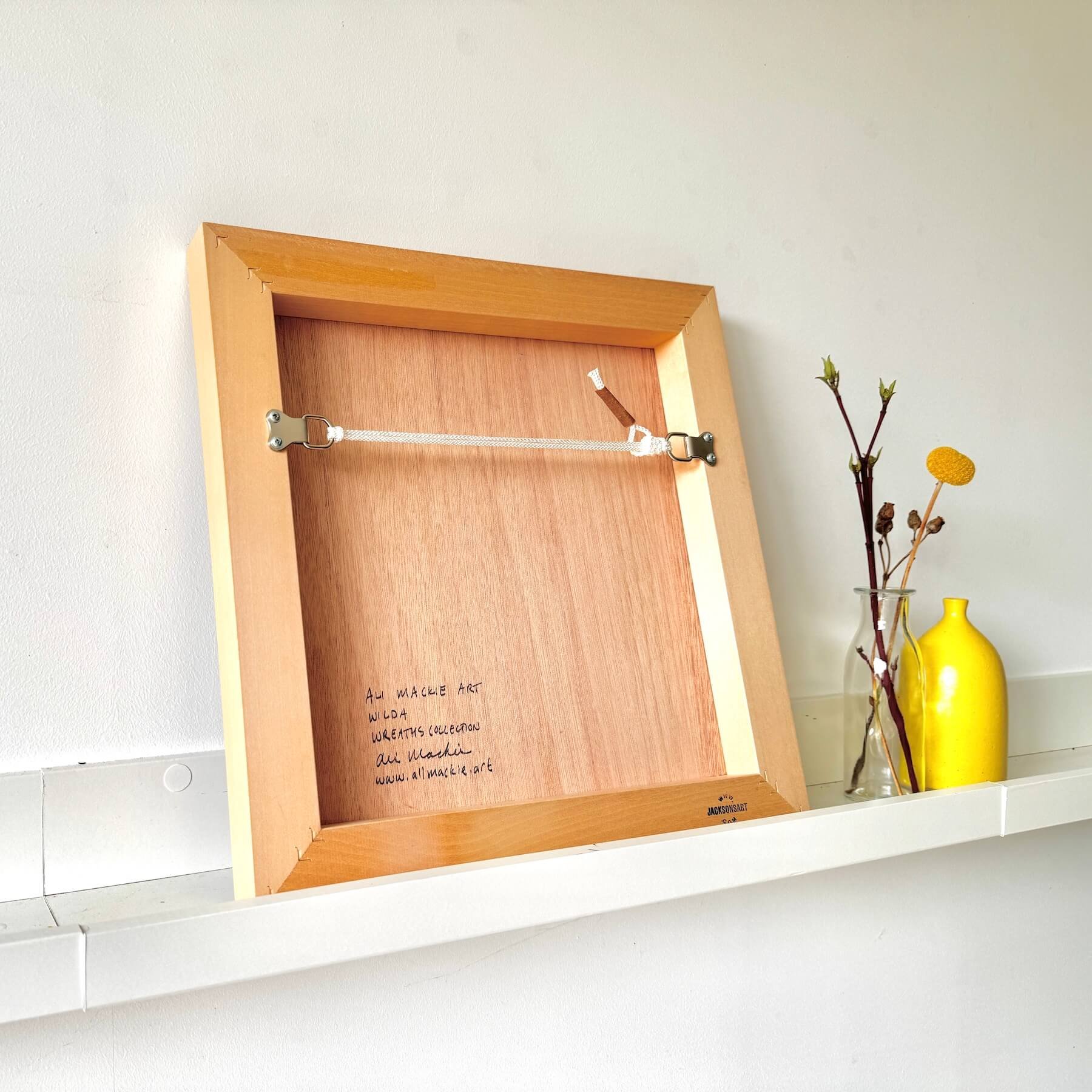 Reverse view of the wooden frame panel showing artist signature Ali Mackie Art, title Wilda, Wreaths Collection, and hanging hardware.