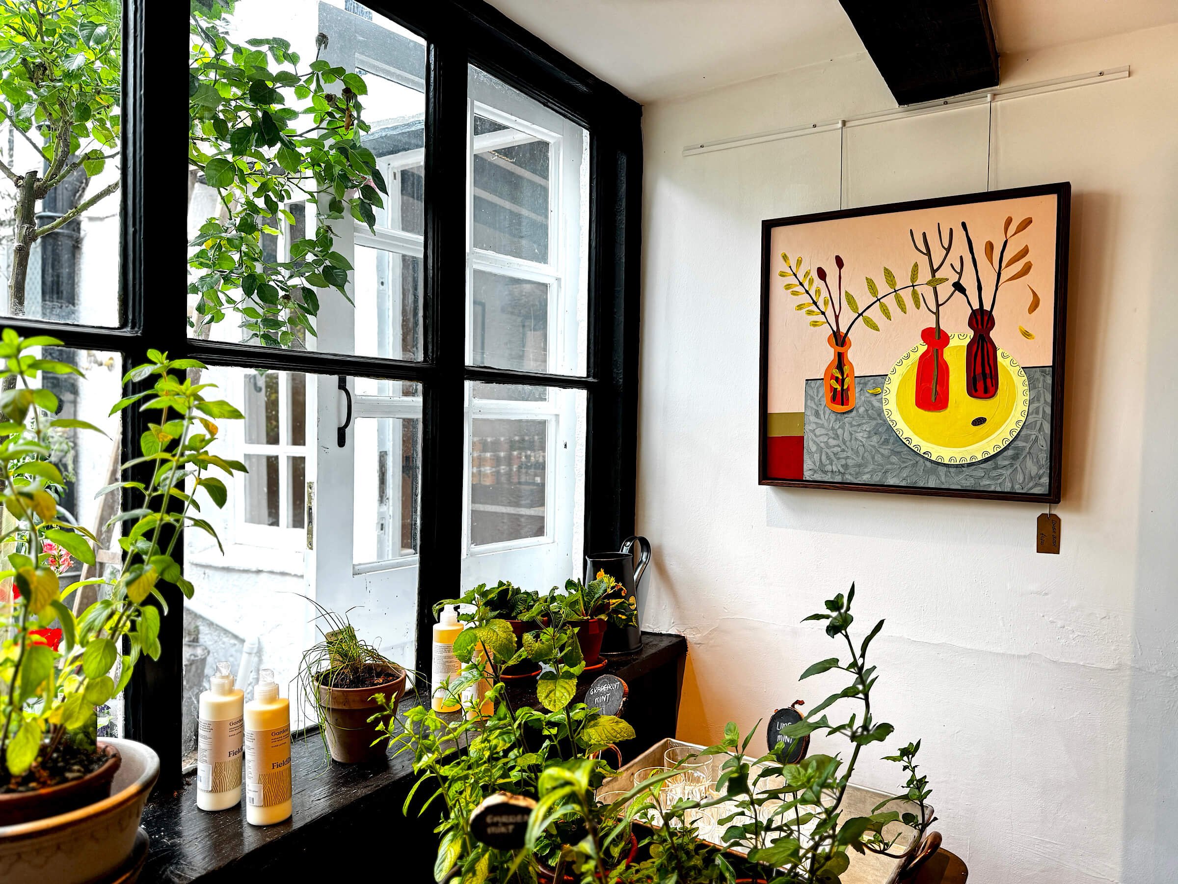 Contemporary folk art painting by Ali Mackie hanging on display in the light-filled interior of The Folde gallery and shop in Old Amersham, Buckinghamshire.