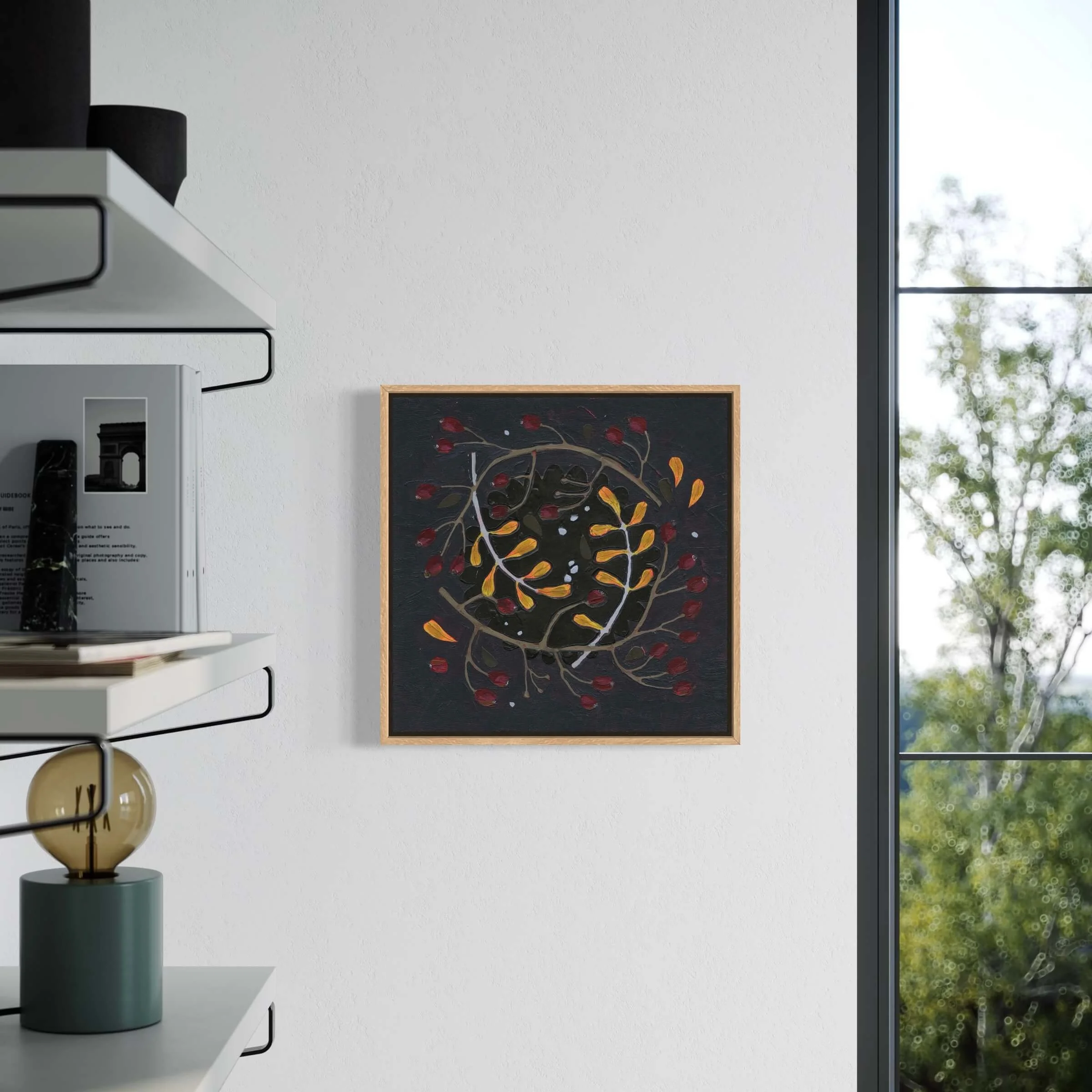 Framed original wreath painting Wilder by Ali Mackie Art hanging on a white wall in a bright room next to a window and open shelving unit.