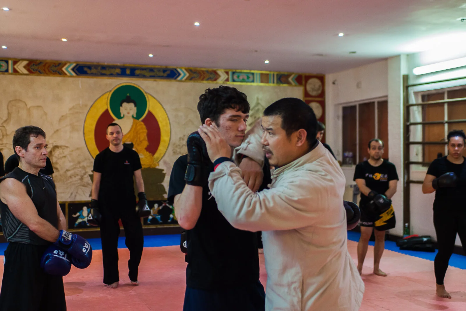 Martial arts training in a dojo with a man practicing a technique on a younger man while others observe.