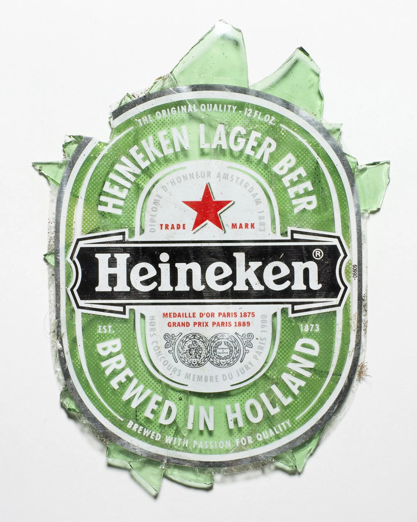 Crushed Heineken beer bottle label with green color and logo, surrounded by broken glass fragments.