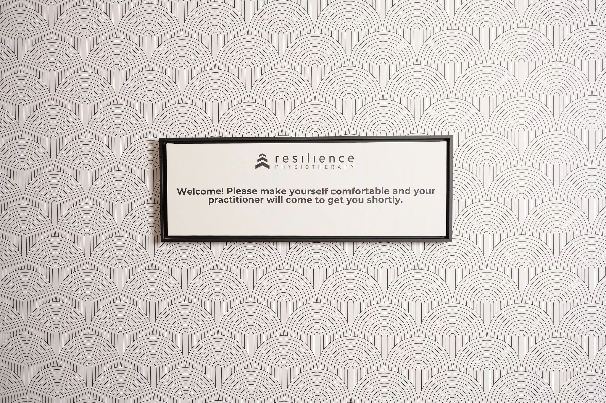 Sign on patterned wall that reads, 'resilience PHYSIOTHERAPY. Welcome! Please make yourself comfortable and your practitioner will come to get you shortly.'