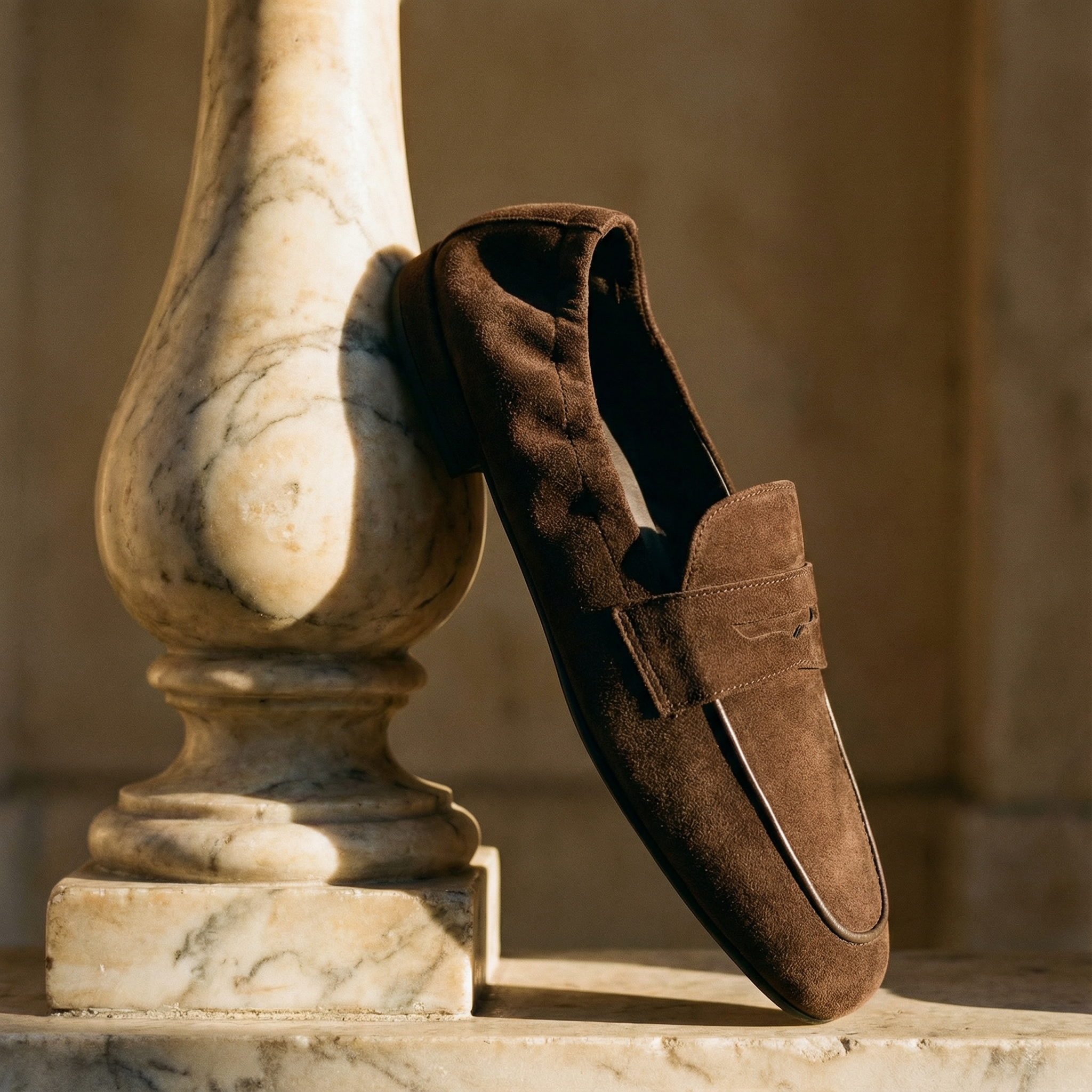 Ein brauner Lederschuh lehnt an einem marmorierten Balusterrand in warmem Sonnenlicht.
