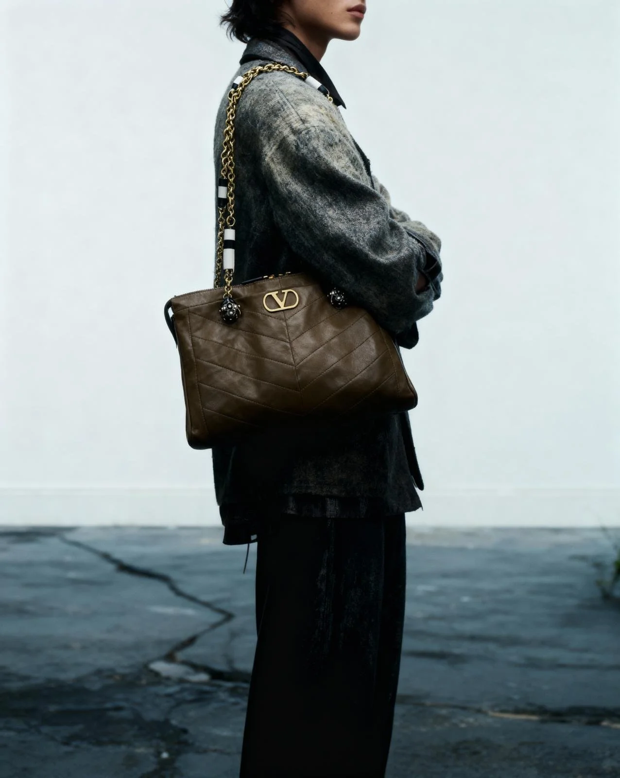 Seitenansicht einer Person, die eine große braune Designer-Tasche mit goldener Schleife trägt, während sie eine dunkle Jacke und schwarze Hose trägt.