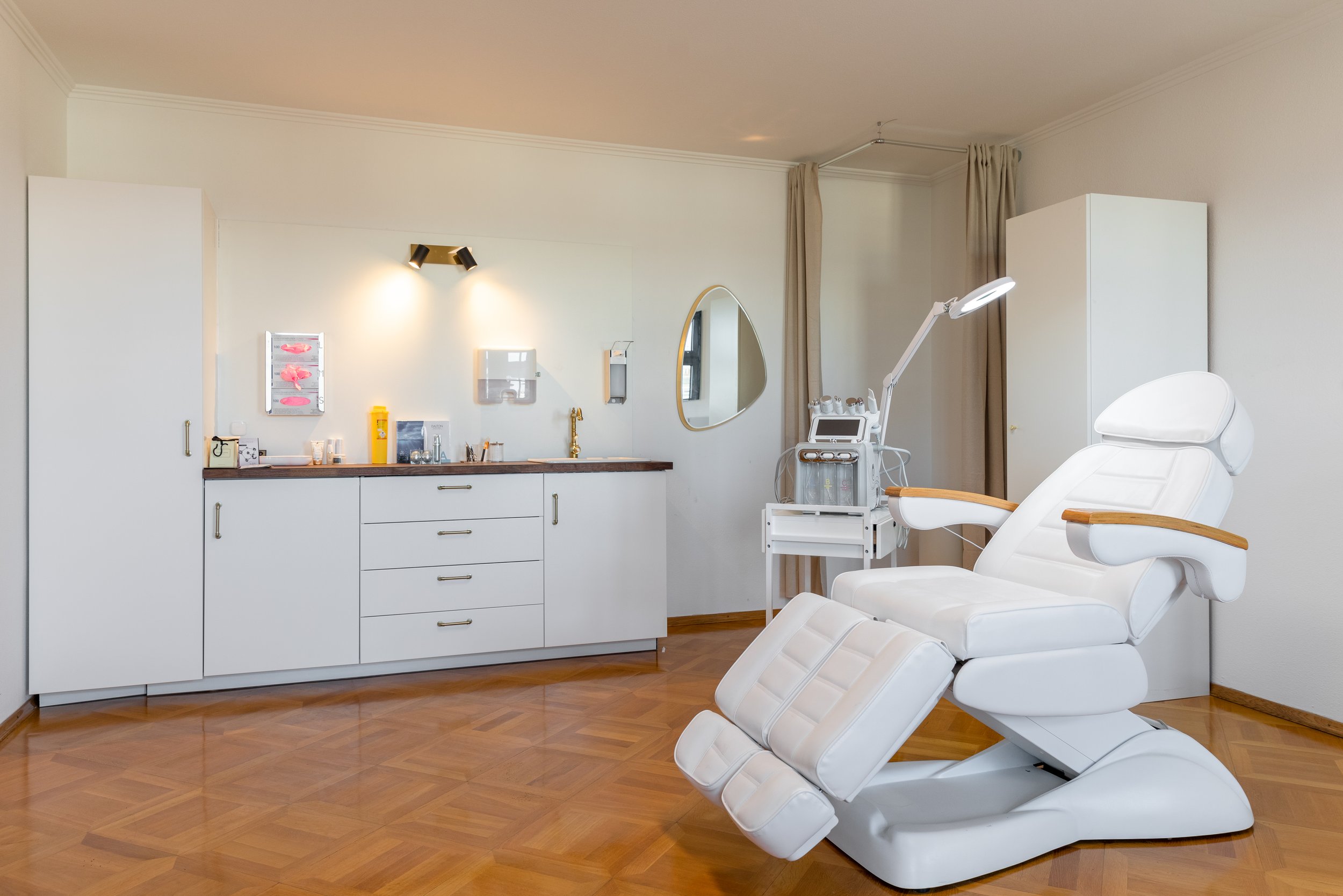 Ein medizinisches Behandlungszimmer mit einem weißen Behandlungsstuhl, medizinischen Geräten, einem Waschbecken, einem Spiegel und verschiedenen medizinischen Utensilien auf einer Holzplatte