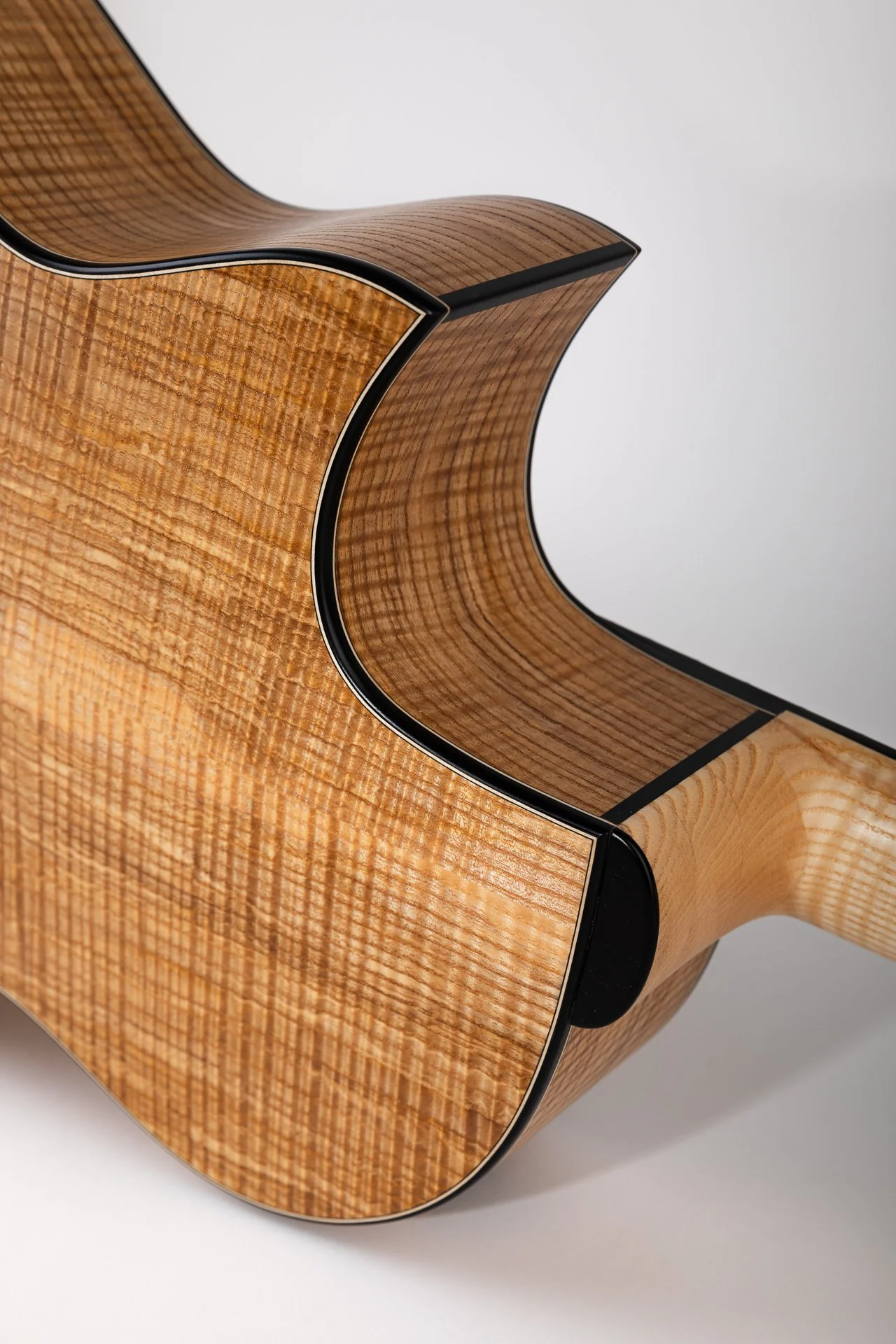 Nahaufnahme einer akustischen Gitarre aus hellbraunem Holz mit schwarzen Details auf weißem Hintergrund.