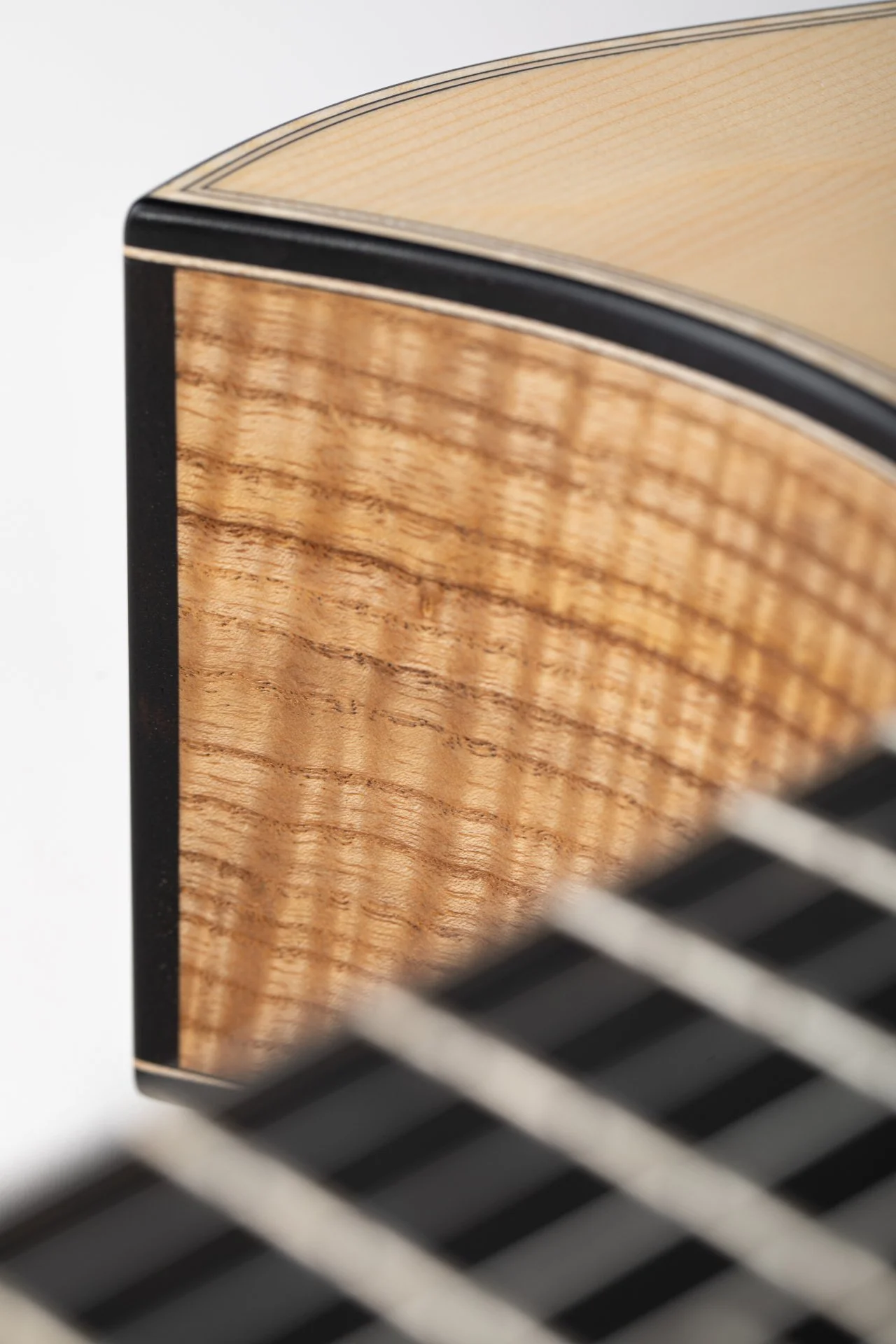 Nahaufnahme eines Akustikgitarren-Korpus mit Holzmaserung und schwarzem Rand im Hintergrund.