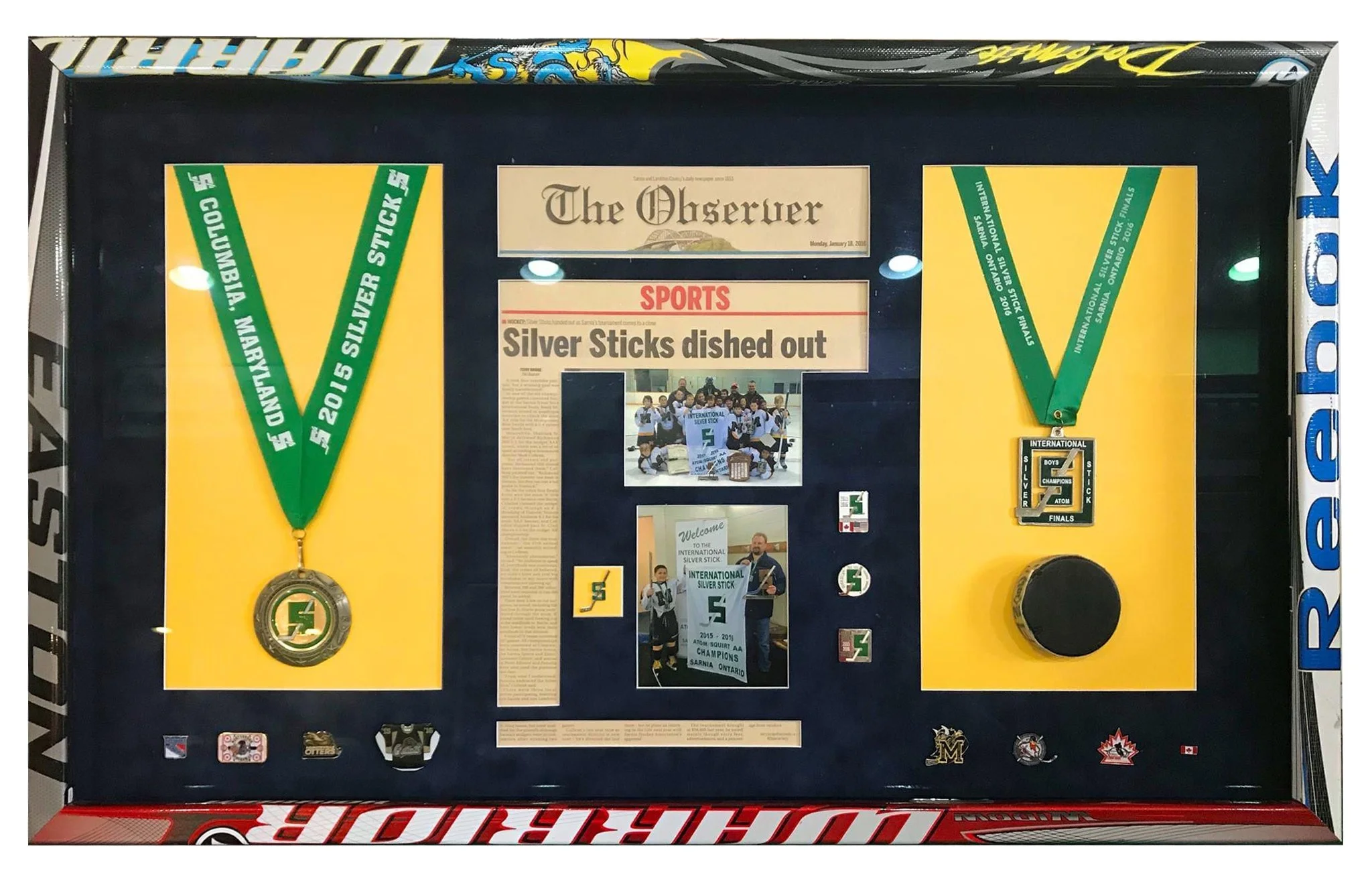 Display case with medals, newspaper clipping, and memorabilia celebrating silver medal achievements at international hockey events.