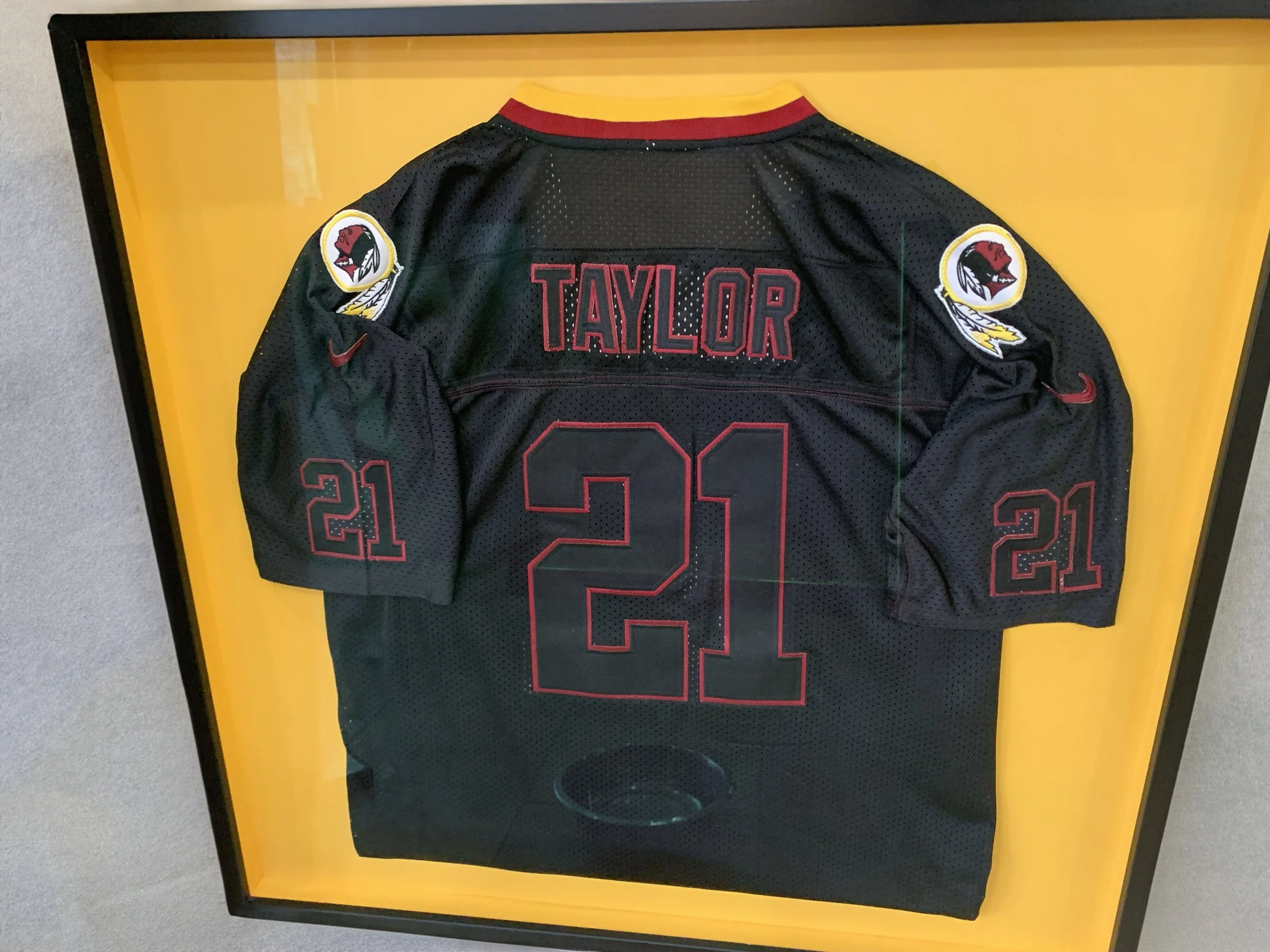 A framed sports jersey with the name "Taylor" and the number "21" on the back, displayed against a yellow background.