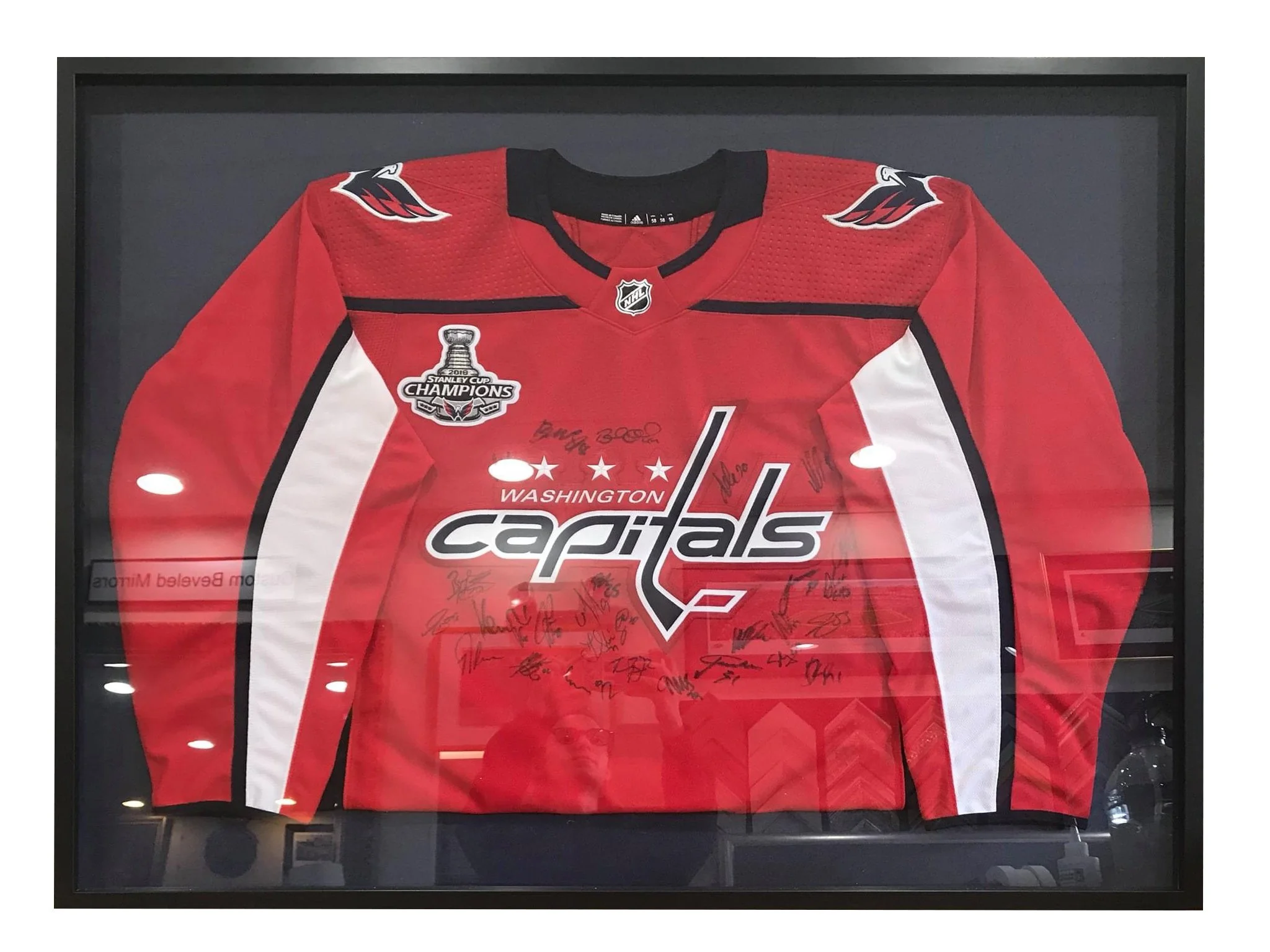 A framed NHL Washington Capitals hockey jersey with team logos, sponsor patches, and signatures, displayed in a glass case.