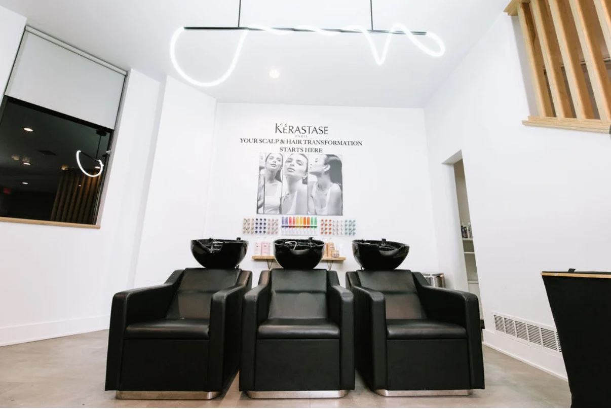 Black shampoo chairs and wash basins beneath a hanging light in the Beauty Culture salon.