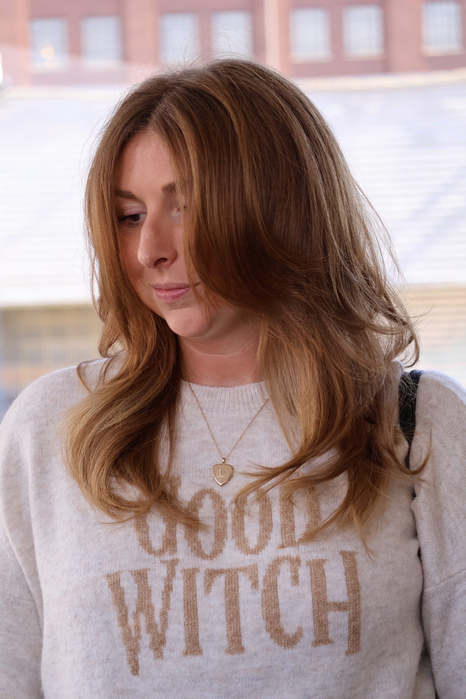 Long warm brown hair with soft layers, worn over a white printed sweatshirt.