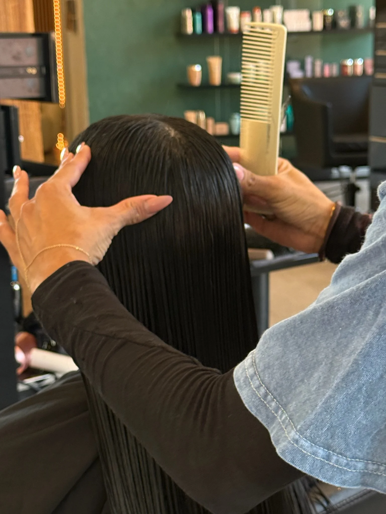 A stylist holds a comb while arranging long, damp dark hair in the salon.