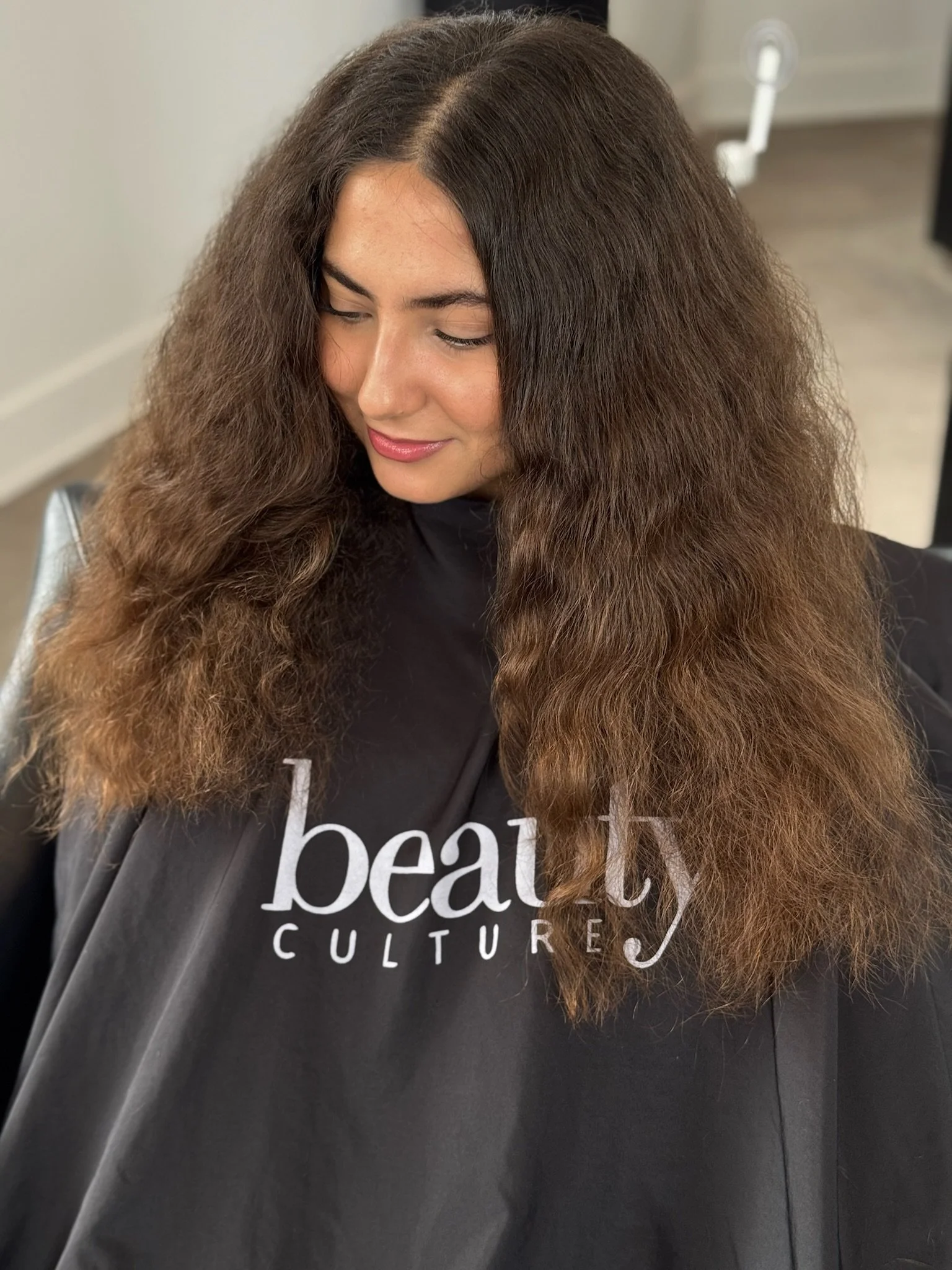 Long brown hair with a soft, full texture worn down over a black Beauty Culture cape.