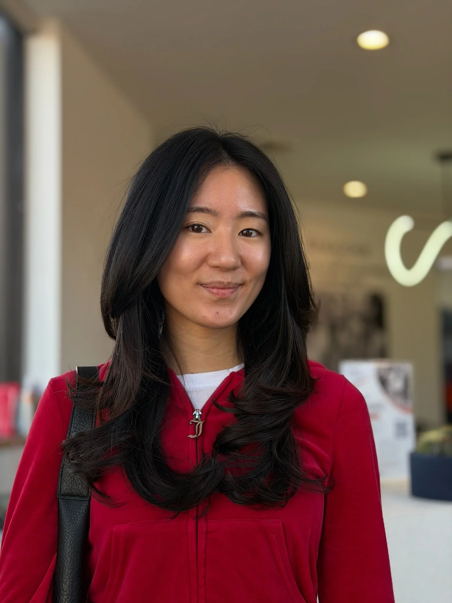 Long dark hair with softly curled layers, worn over a red top.