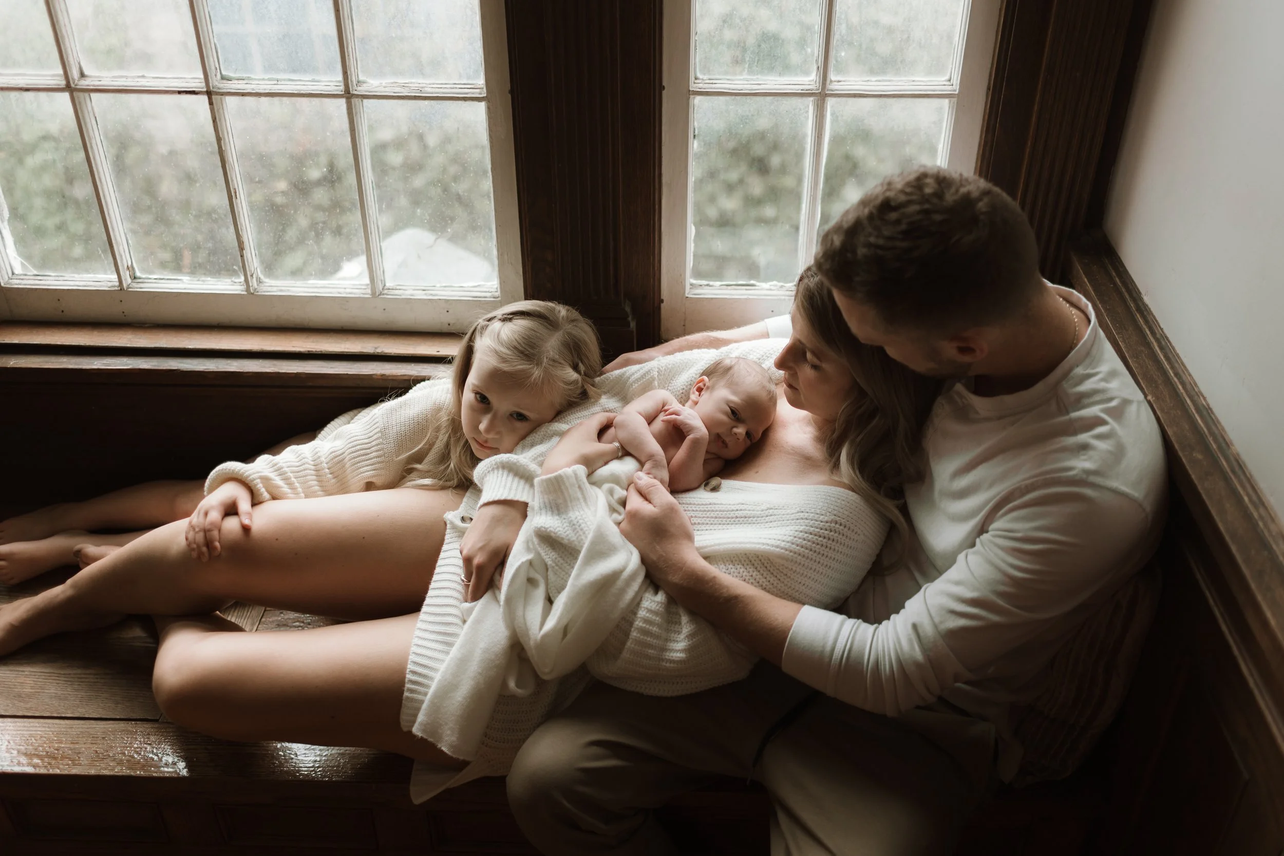 Parents holding their newborn baby at home while their older daughter snuggles in with them