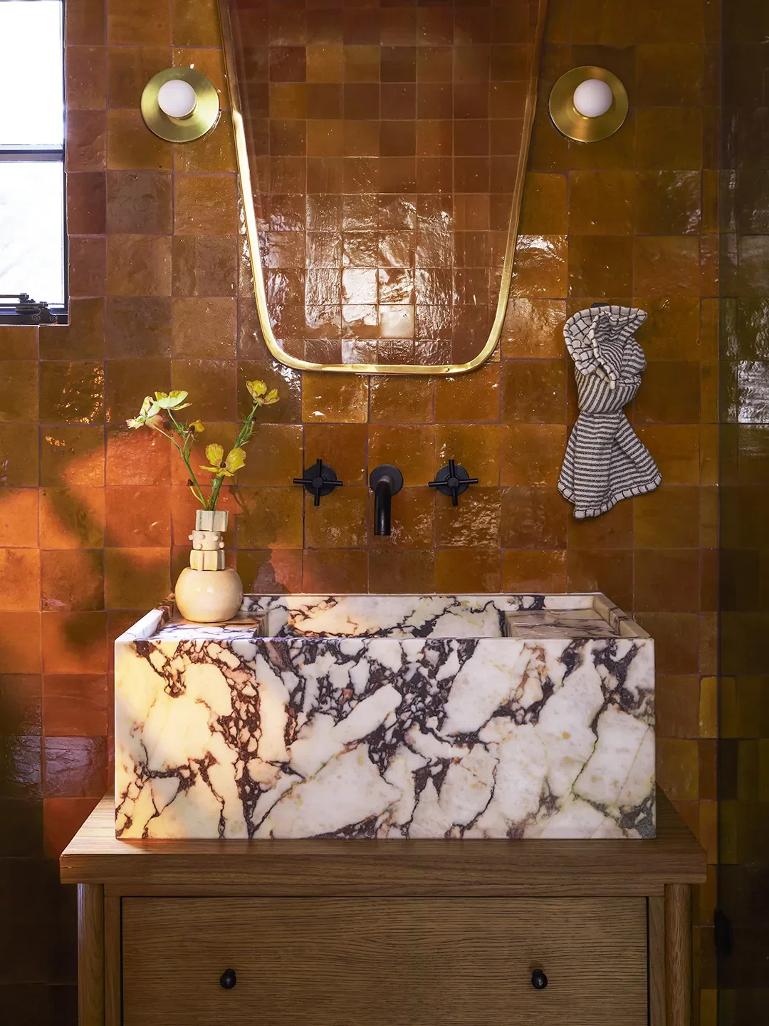 Floor-to-ceiling tiles in a terracotta shade behind a vanity with a mounted marble sink.
