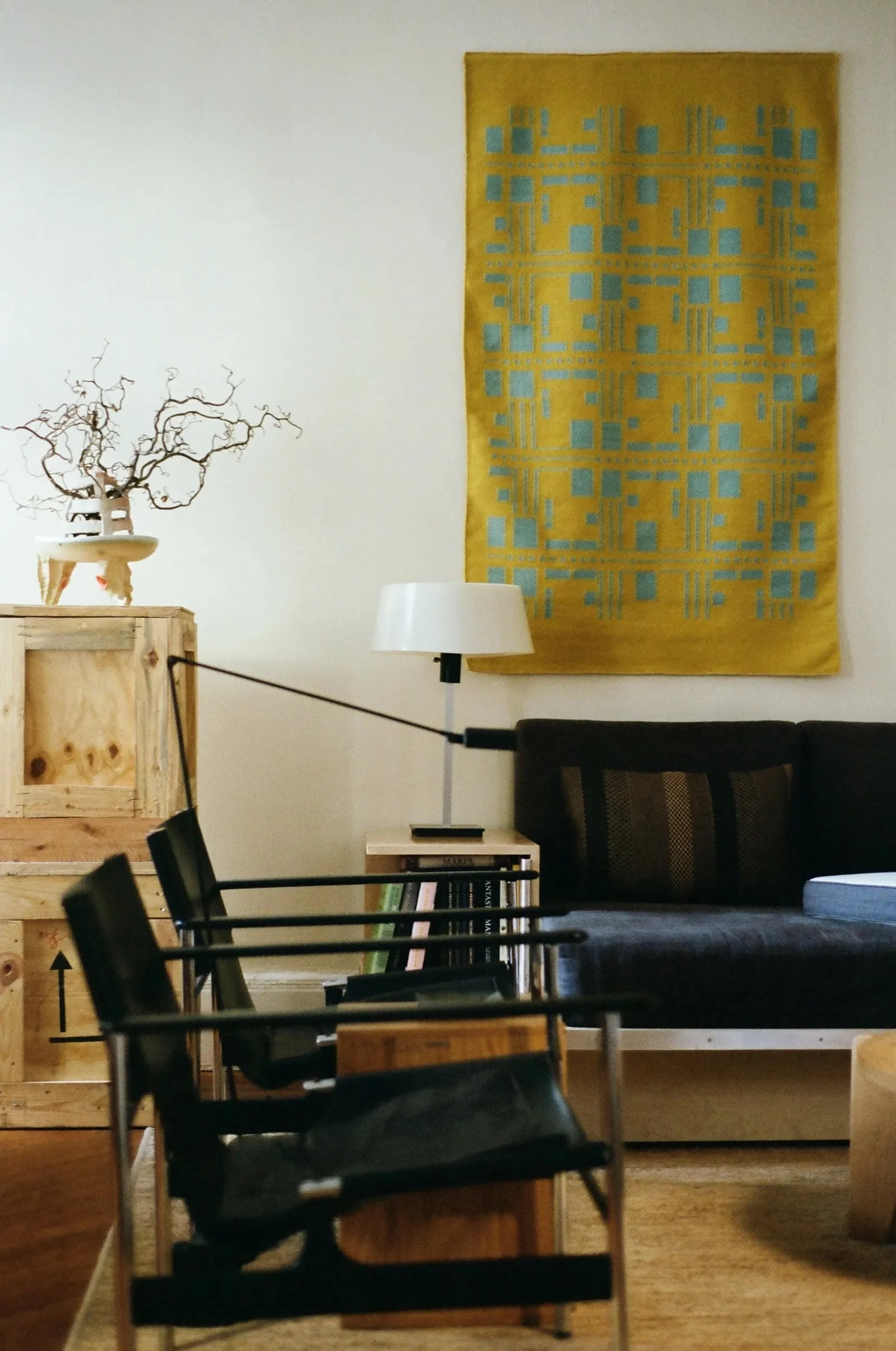 A living room with a black couch, two matching black chairs, and a yellow-and-blue tapestry over the couch.