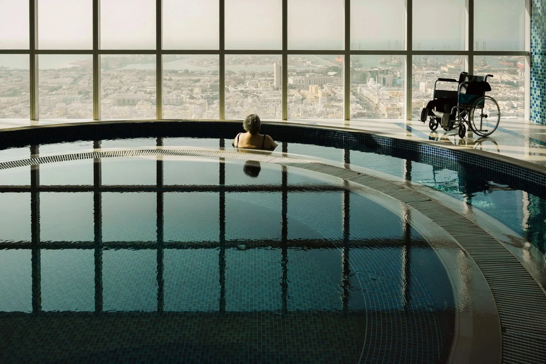 A woman in an indoor pool with a wheelchair beside the ledge.