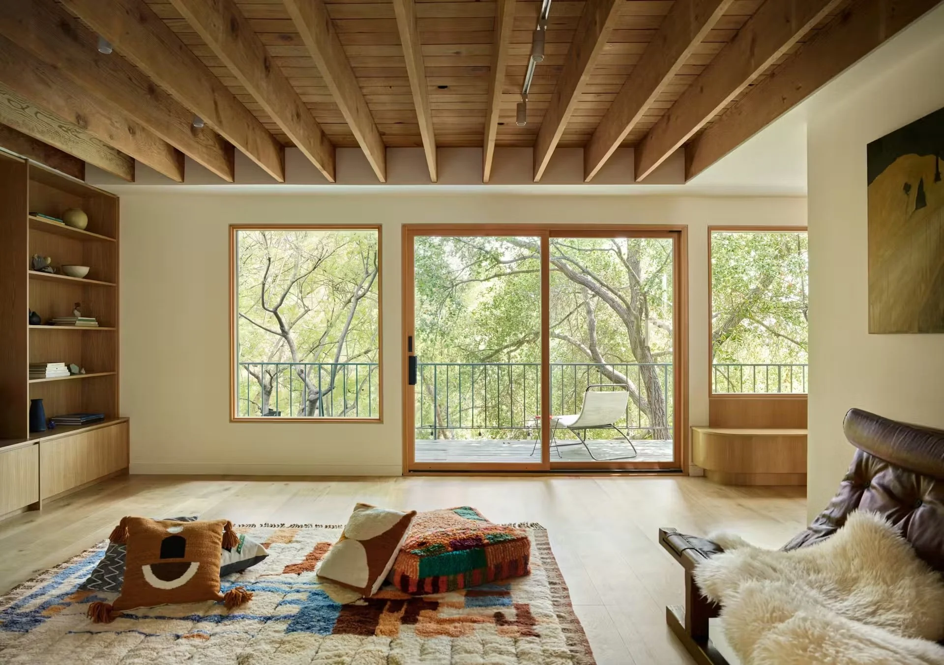 A living room with an exposed beam ceiling overlooking green trees.
