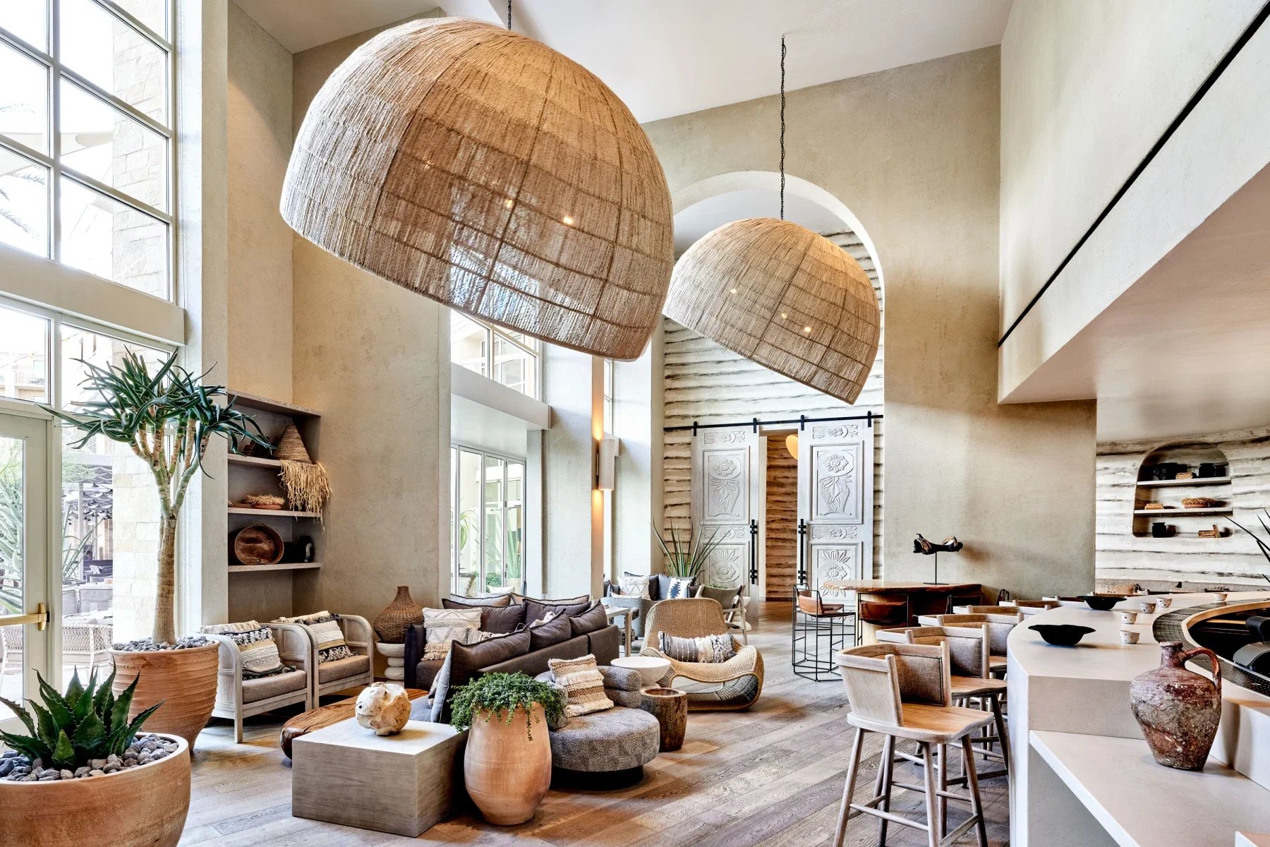 A neutral lobby with two large, woven pendant lights over seating options near a bar.