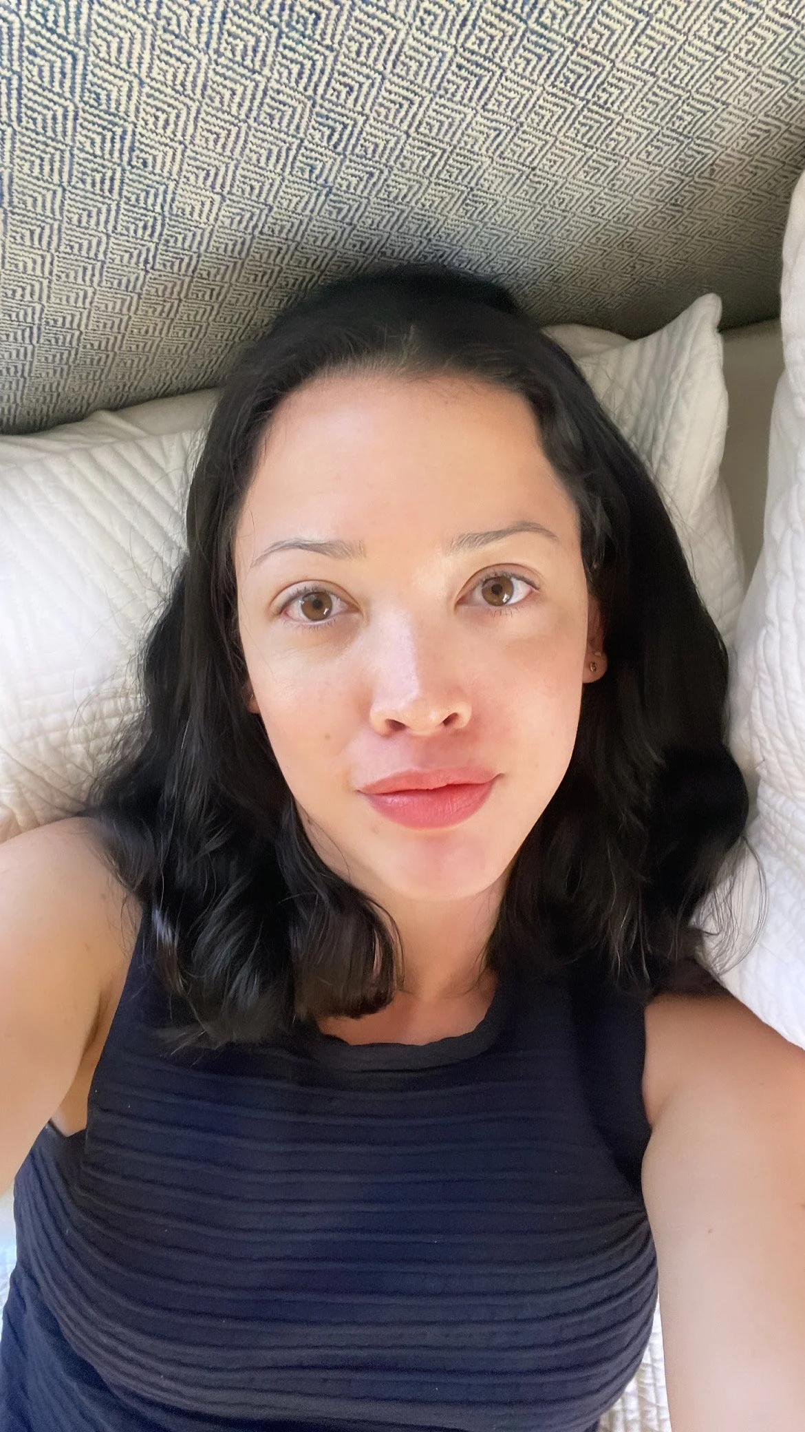 I have clear, pale skin and dark curly hair. I'm smiling for a selfie wearing a blue tank top.
