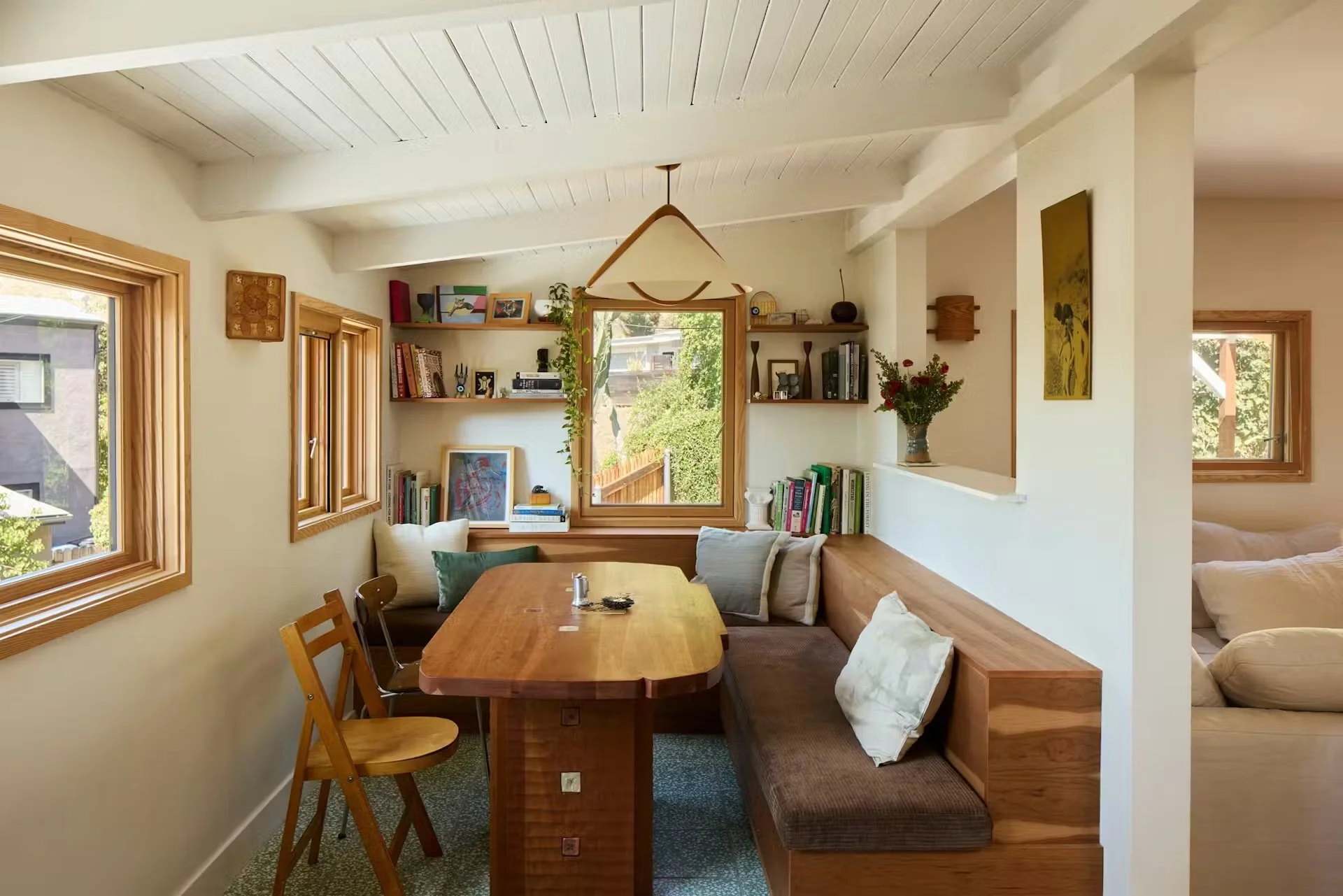 A dining banquette with a wood bench and table surrounded by books and artwork.