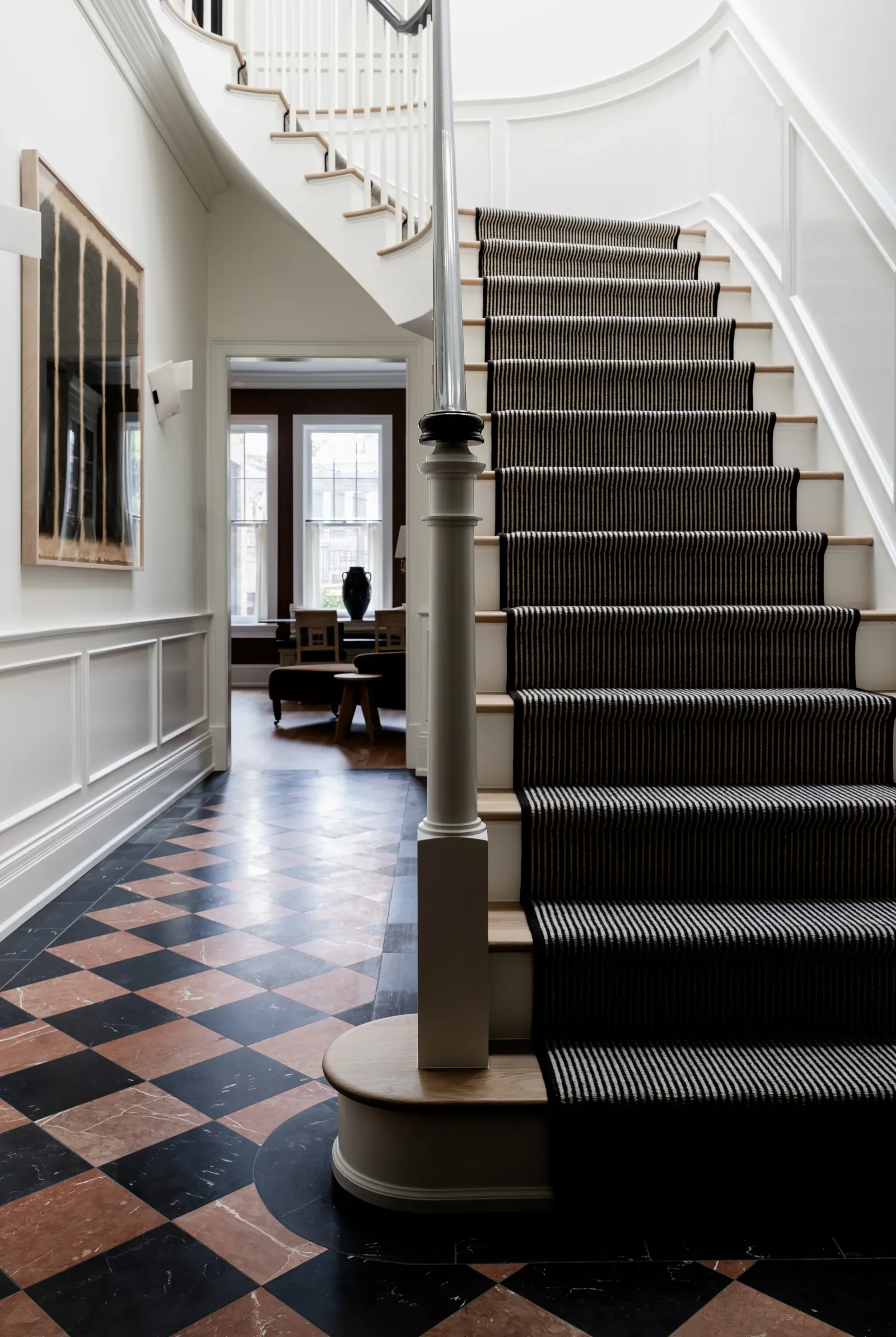 A staircase with a black-and-white striped runner and a marble floor at the base.