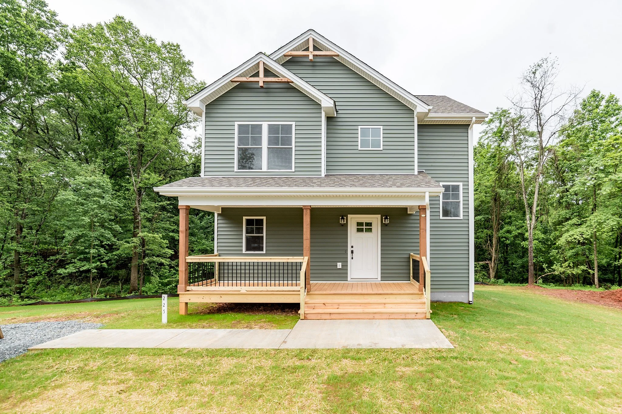 Two-story house with green siding, a covered front porch, white door, and surrounded by trees and grass.
