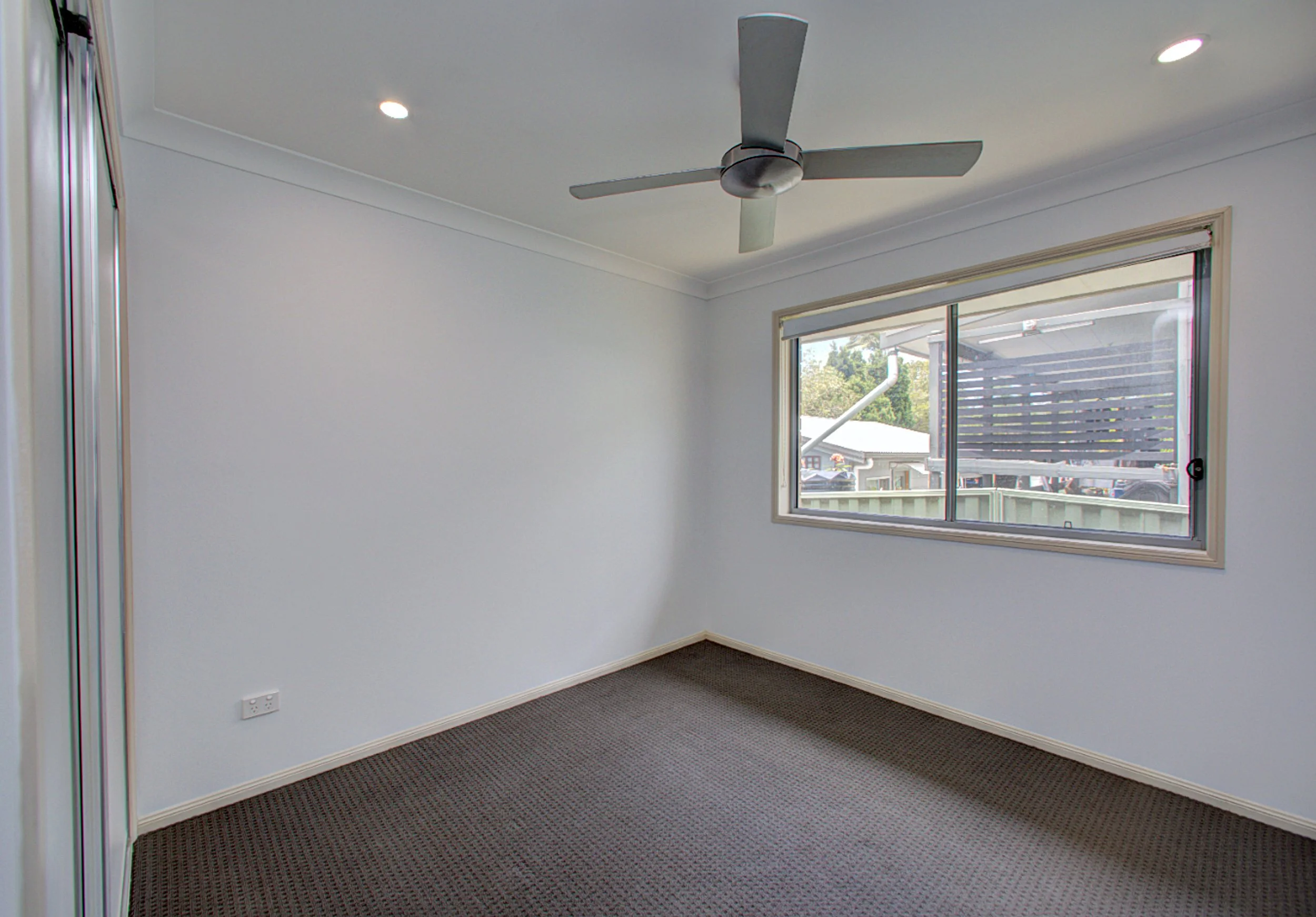 Empty room with white walls, a window facing outside, a ceiling fan, and recessed lighting.
