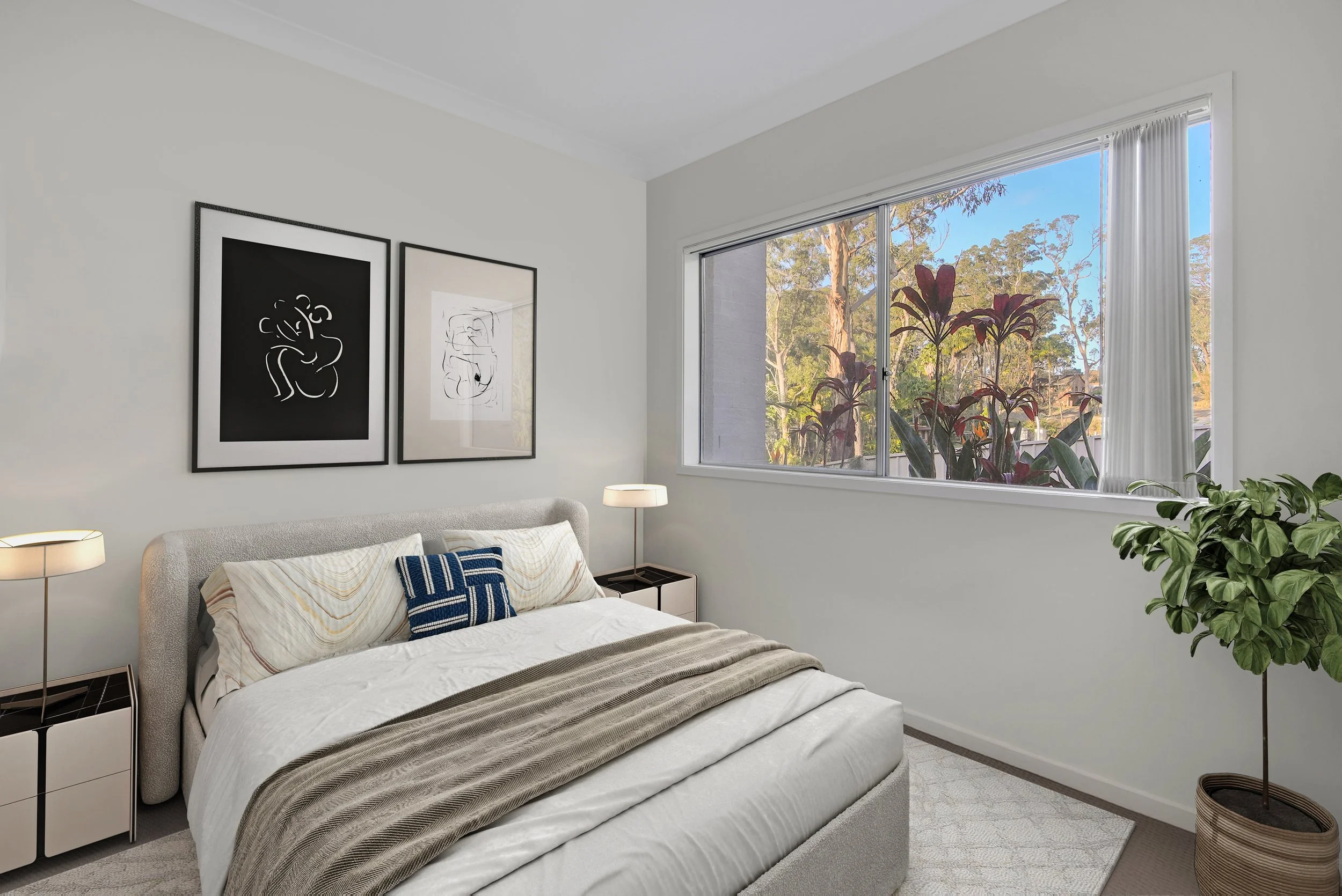 A bright, minimalist bedroom with a large window showing trees outside. The room has a beige upholstered bed with white and cream bedding, a blue accent pillow, and two matching nightstands with modern lamps. There is black-and-white artwork on the w
