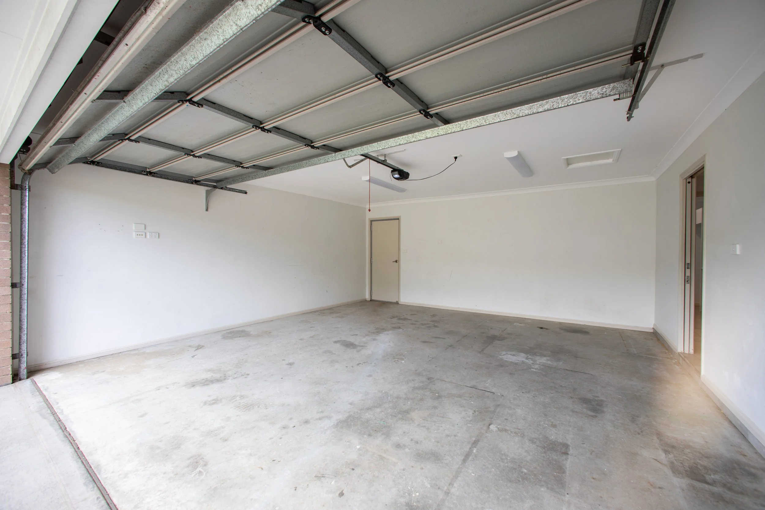 Empty garage with concrete floor, white walls, and a partially open overhead garage door.
