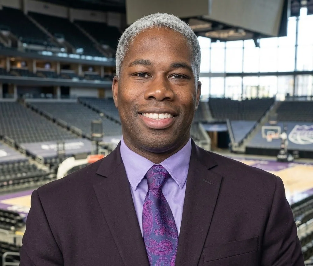 A man in a suit and tie smiling in an empty basketball arena.