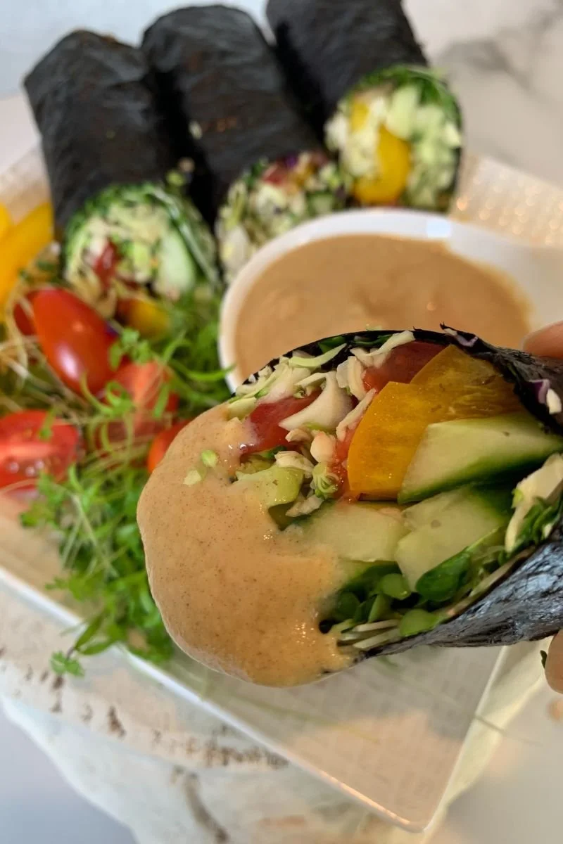 Raw vegan sushi hand roll filled with avocado and vegetables and dipped in sauce.