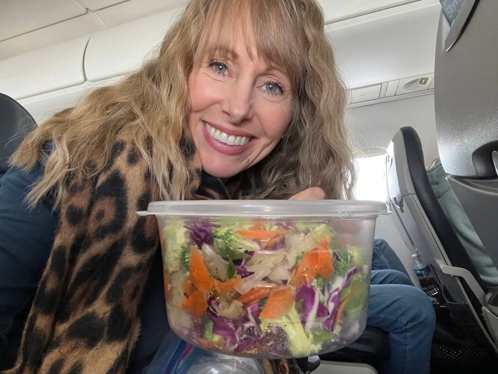 Michelle of Green Food Crush holding a packed vegetable salad on an airplane while following Dr. Brooke Goldner's Goodbye Autoimmune Protocol