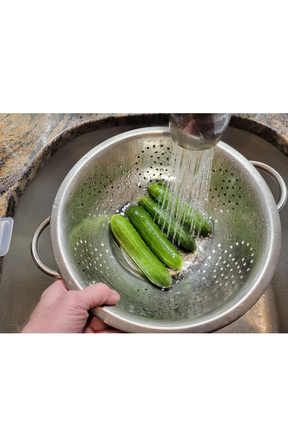 Washing cucumbers in a metal colander under running water.