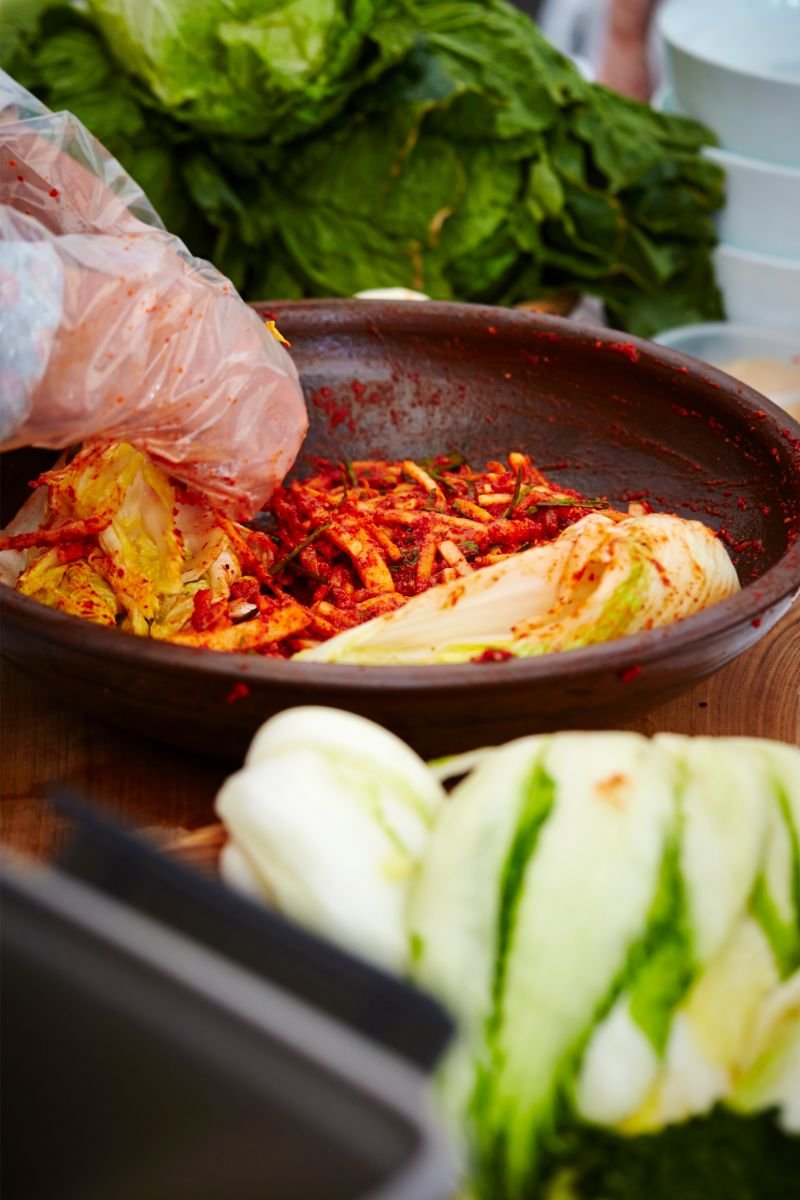 Napa cabbage and vegetables being mixed with red kimchi seasoning by hand.