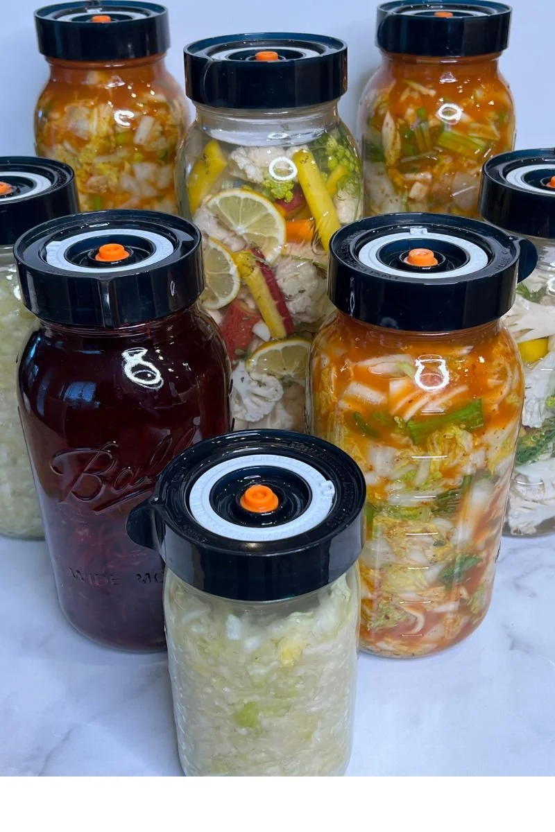 Assorted homemade fermented vegetables in glass jars fitted with fermentation lids.