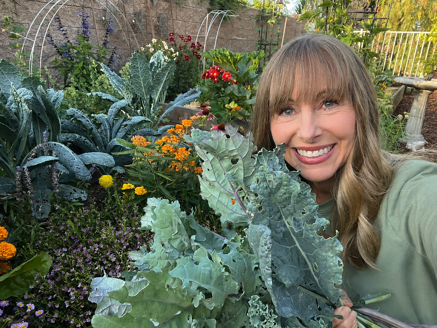 Michelle smiling in her garden beside large kale plants and other leafy greens.