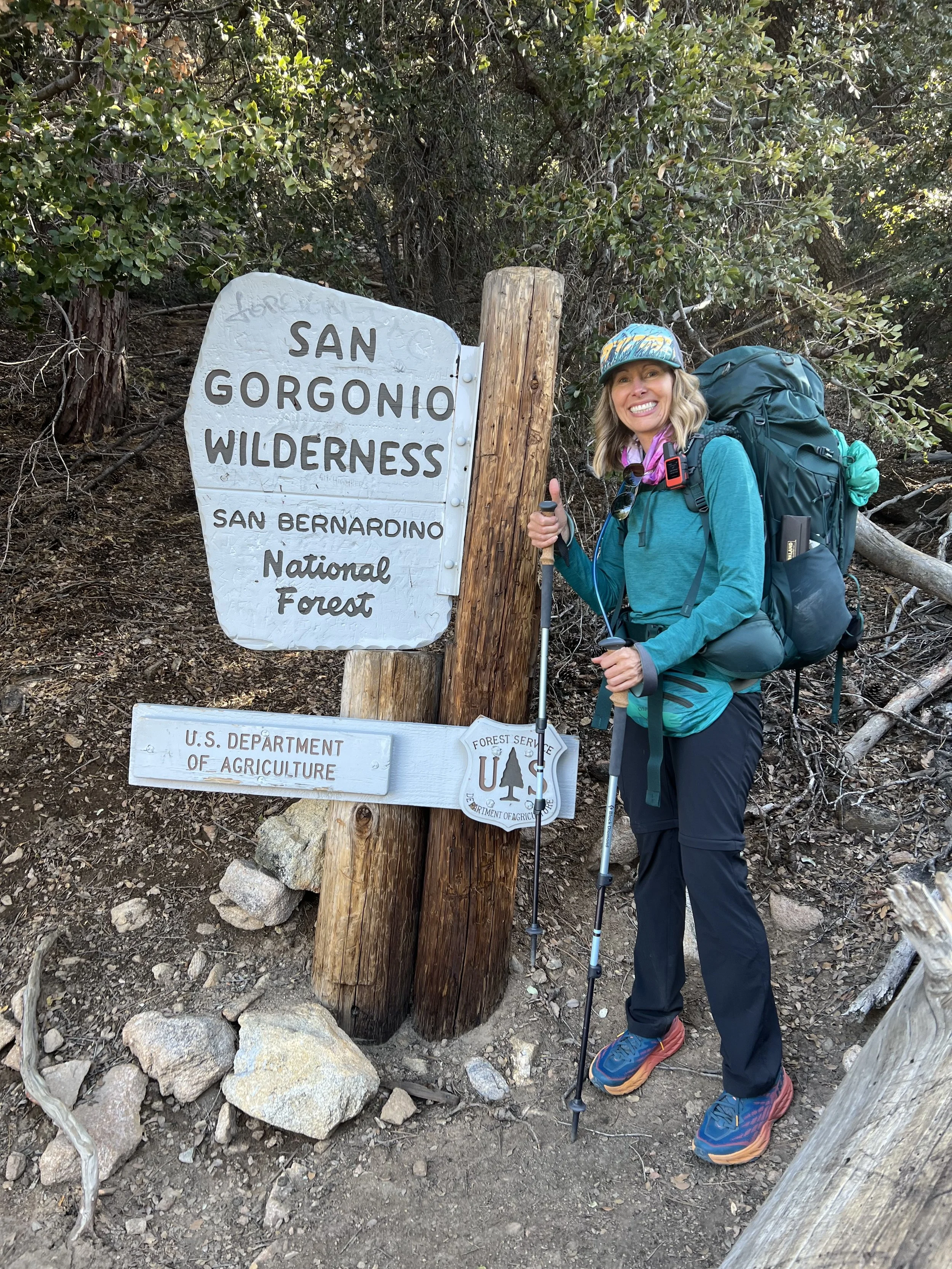 Michelle standing beside the San Gorgonio wilderness sign with a backpack, preparing for a backpacking trip in the San Bernardino National Forest