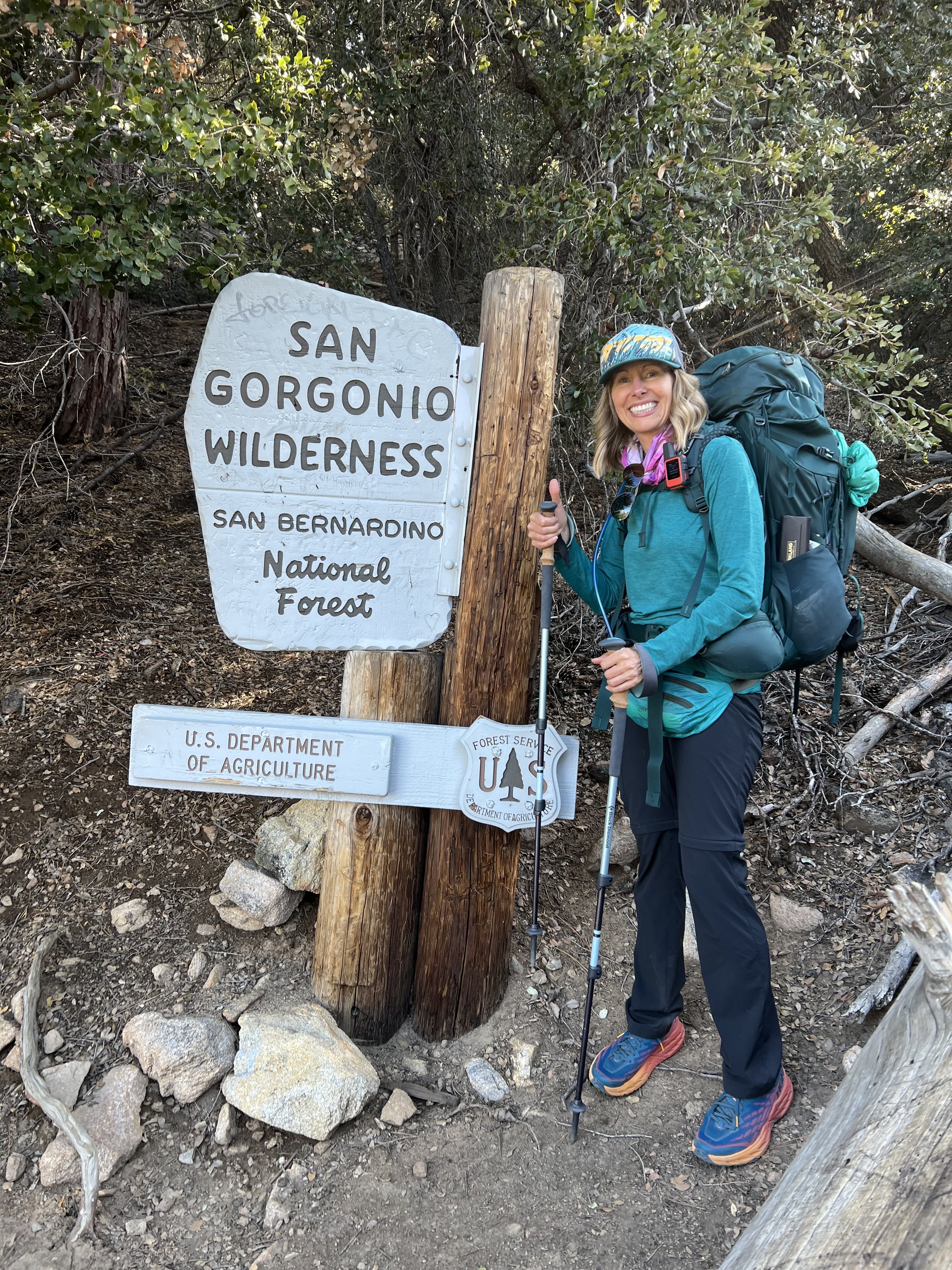 Michelle standing beside the San Gorgonio wilderness sign with a backpack, preparing for a backpacking trip in the San Bernardino National Forest