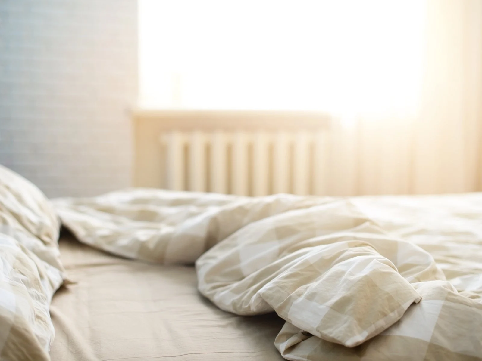 unmade bed with light-colored bedding in soft morning light