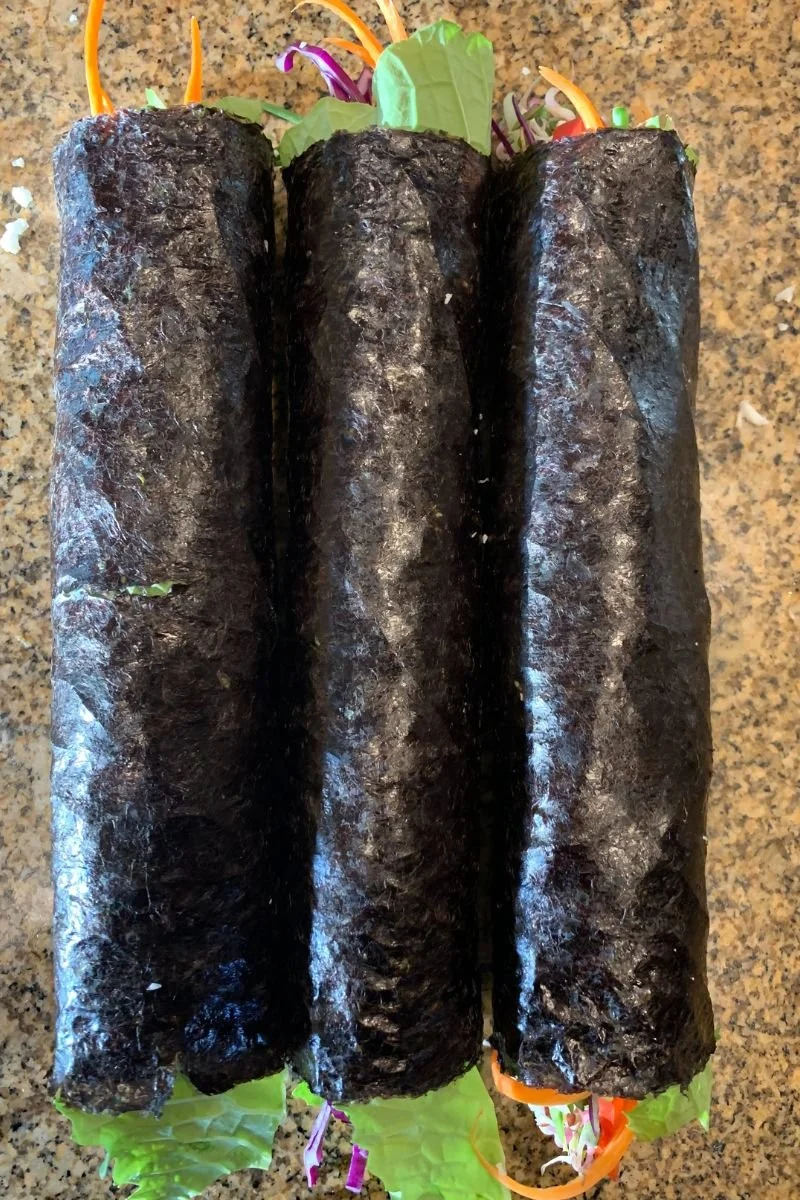 Three freshly rolled raw vegan sushi rolls wrapped in nori
