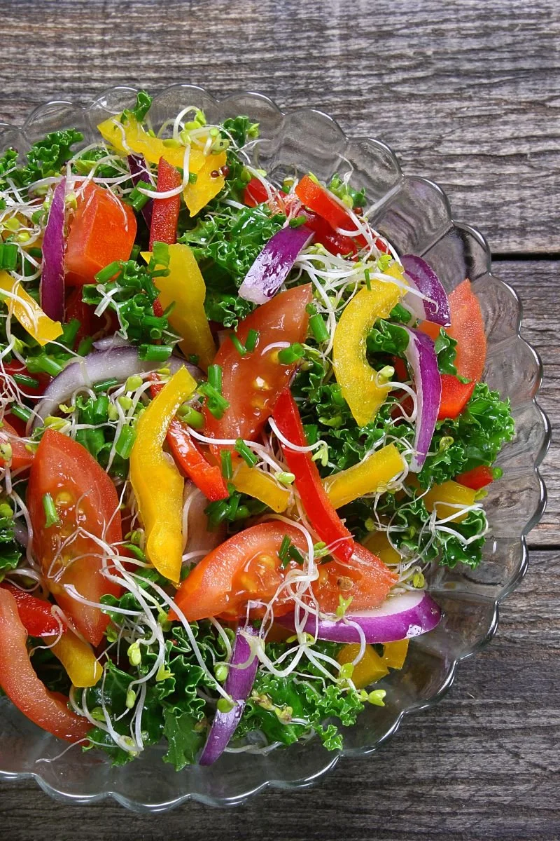 Colorful salad with broccoli sprouts, kale, tomatoes, bell peppers, and red onion.