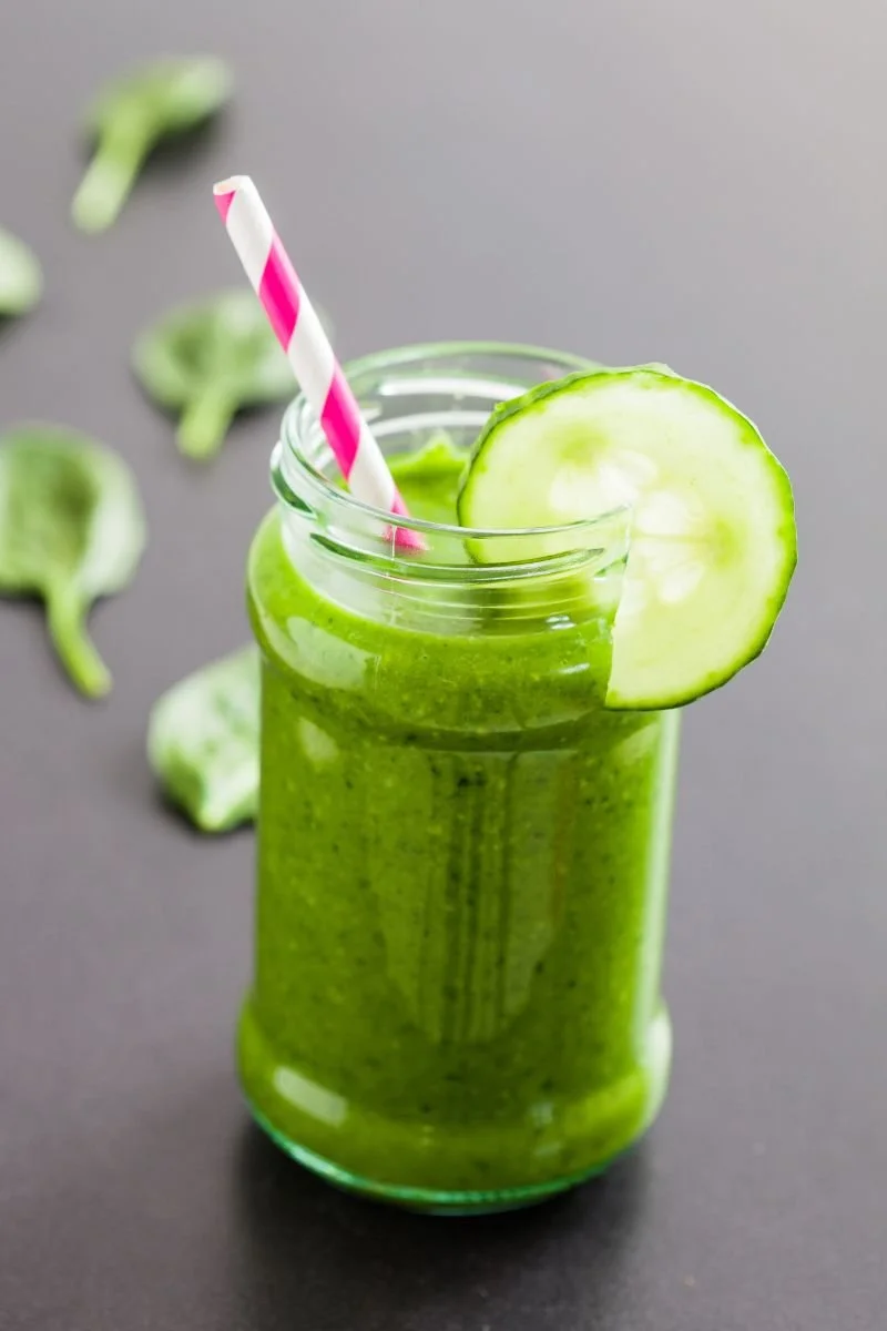 Green smoothie in a glass jar with cucumber garnish.